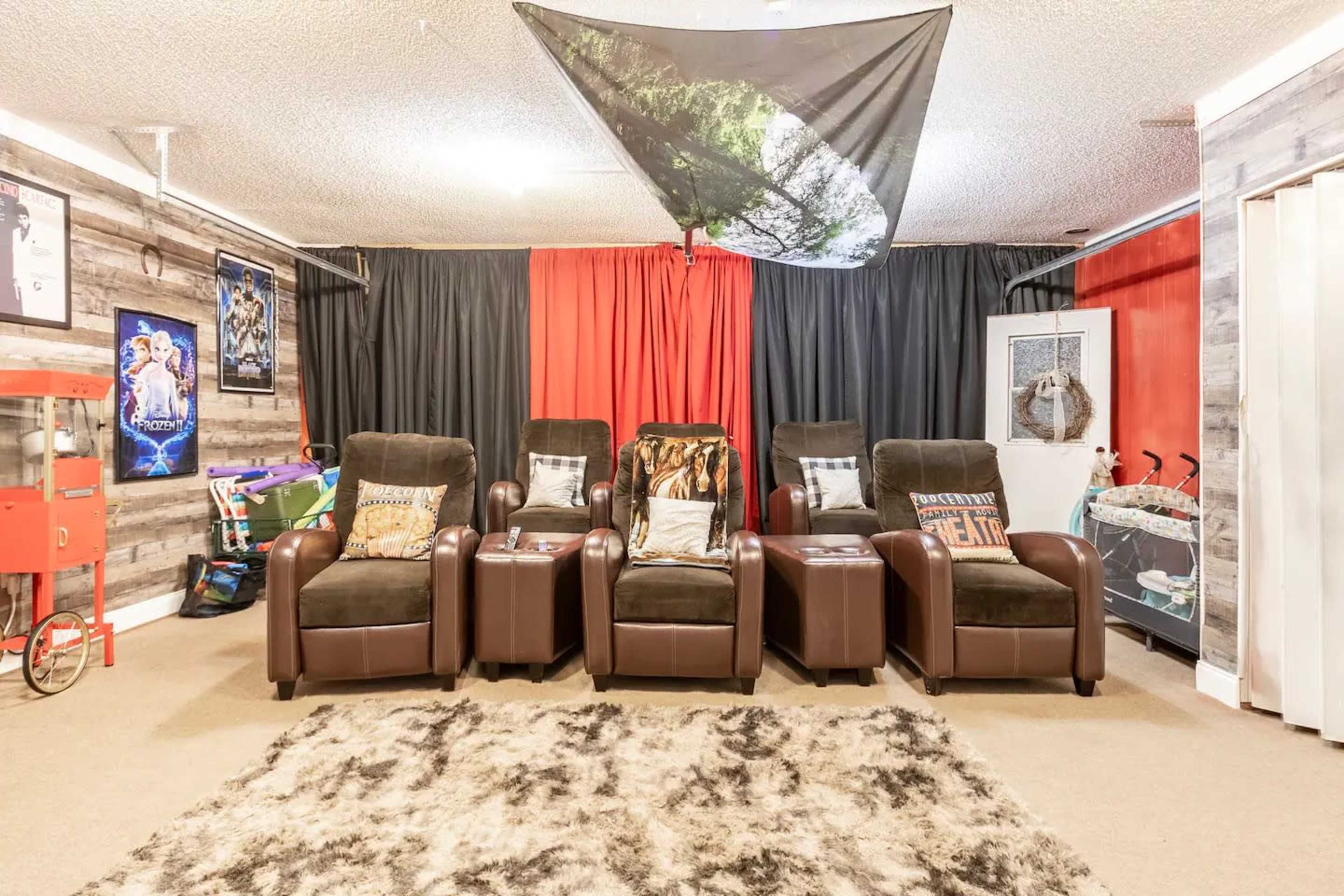 A home theater setup featuring four recliner seats arranged in front of a black and red curtain backdrop, with a decorative rug on the floor.