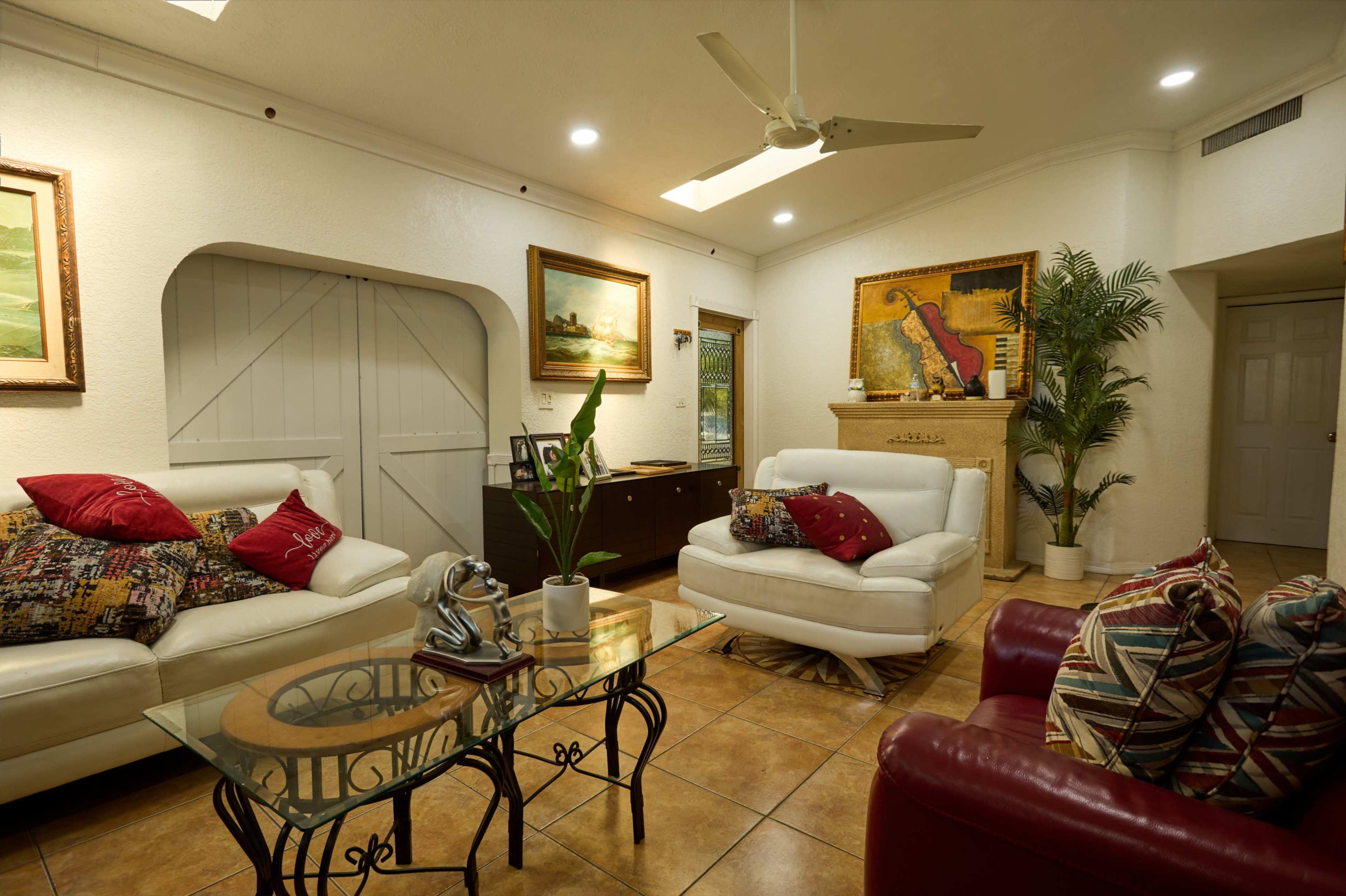The image shows a living room with two white sofas and a red armchair, a glass coffee table, and artwork on the walls.