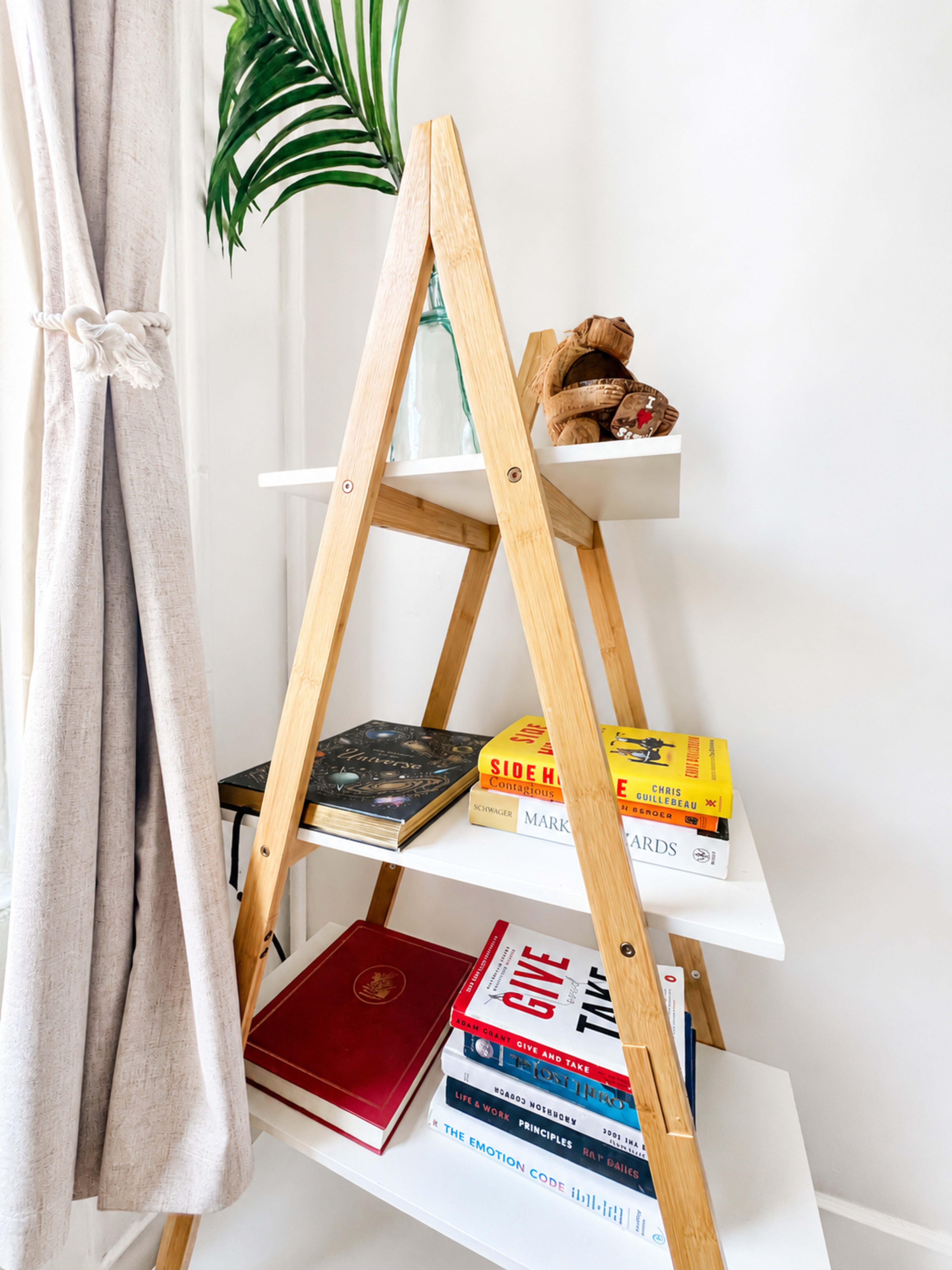 A wooden ladder-style bookshelf displays a variety of colorful books and decorative items against a white wall.