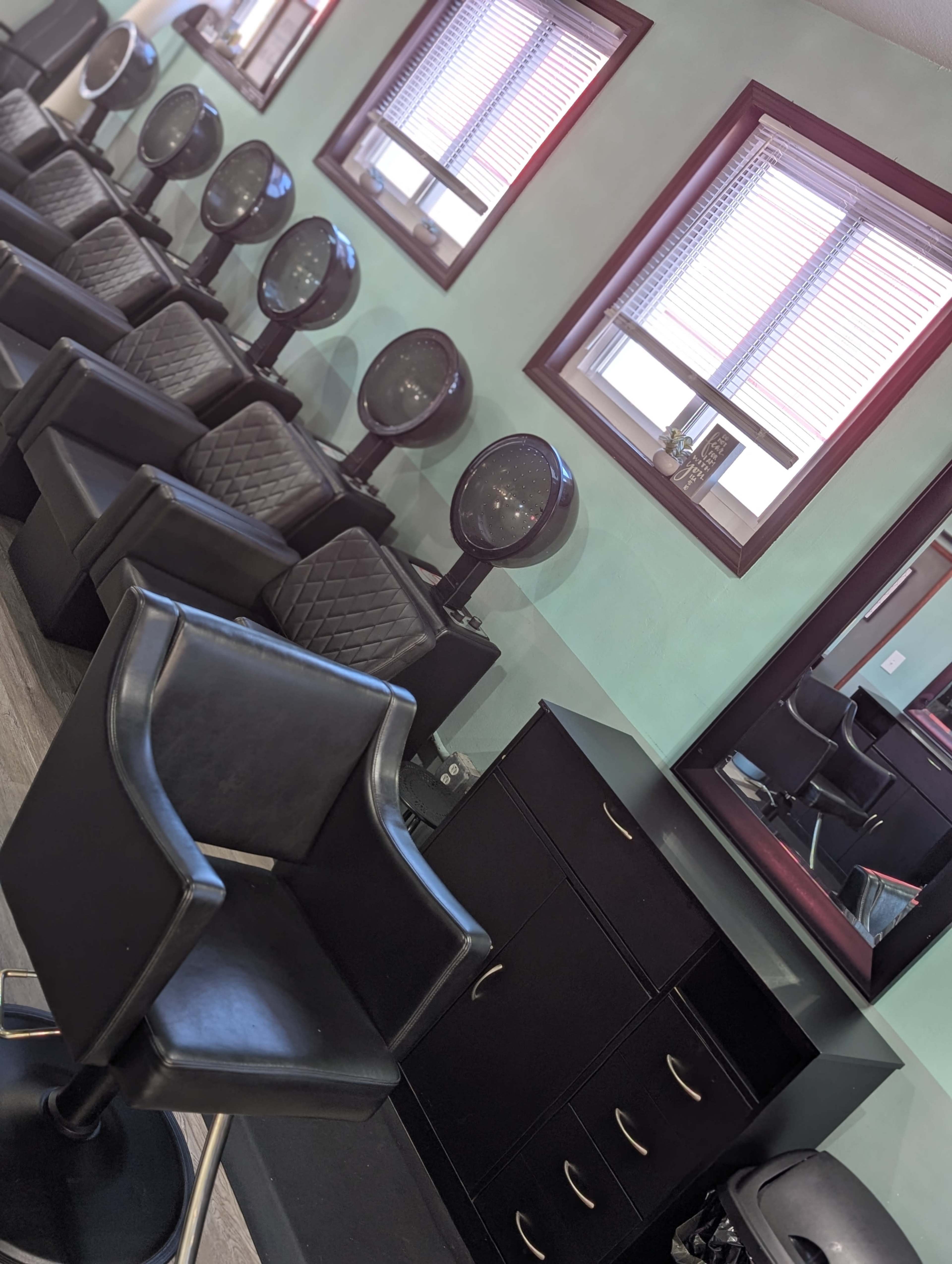 The image shows a salon interior with black chairs, hairdryers, and a mirror along the wall, illuminated by natural light from the windows.