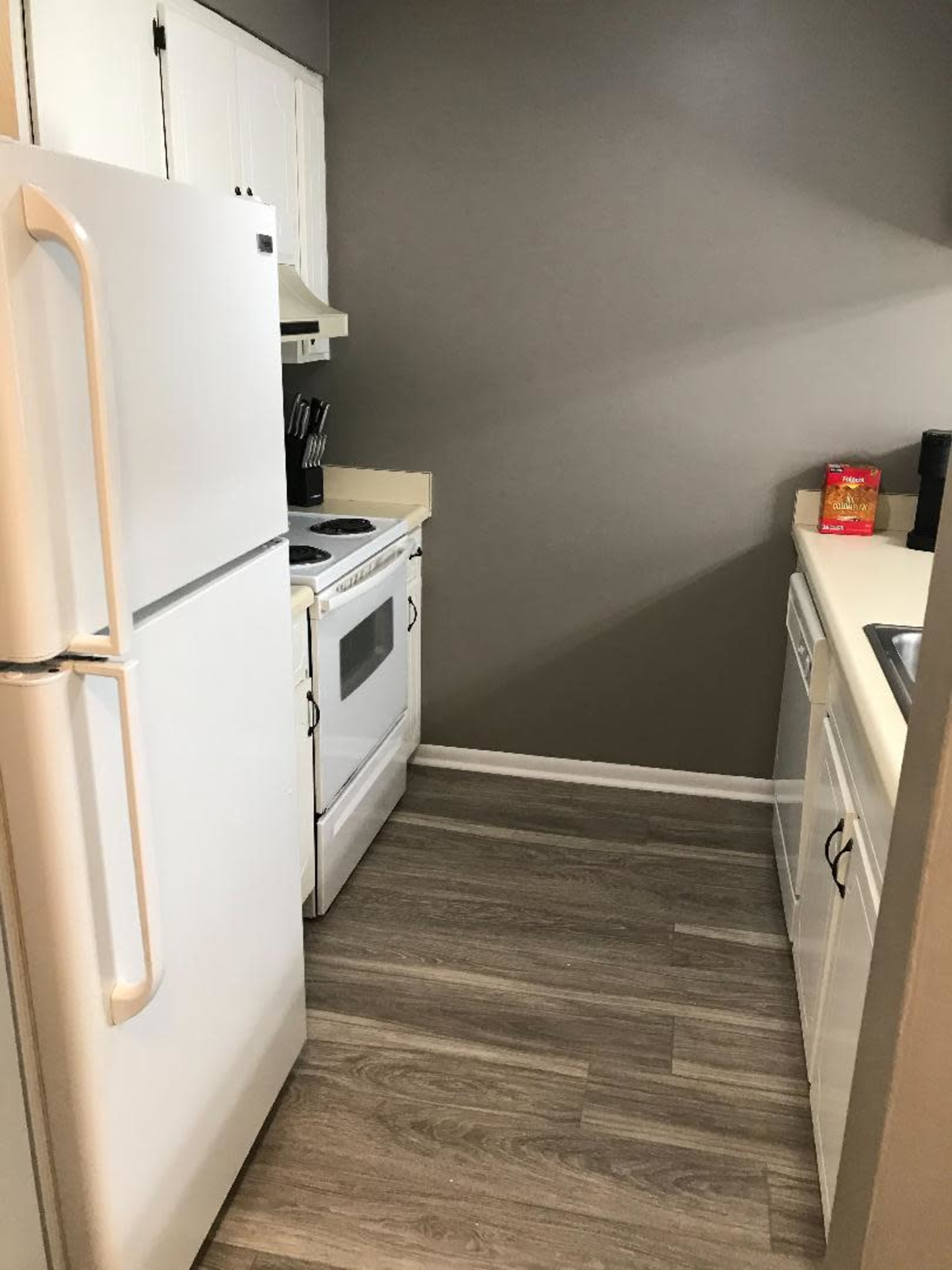 A compact kitchen with a refrigerator, stove, and sink, featuring light-colored cabinets and laminate flooring.