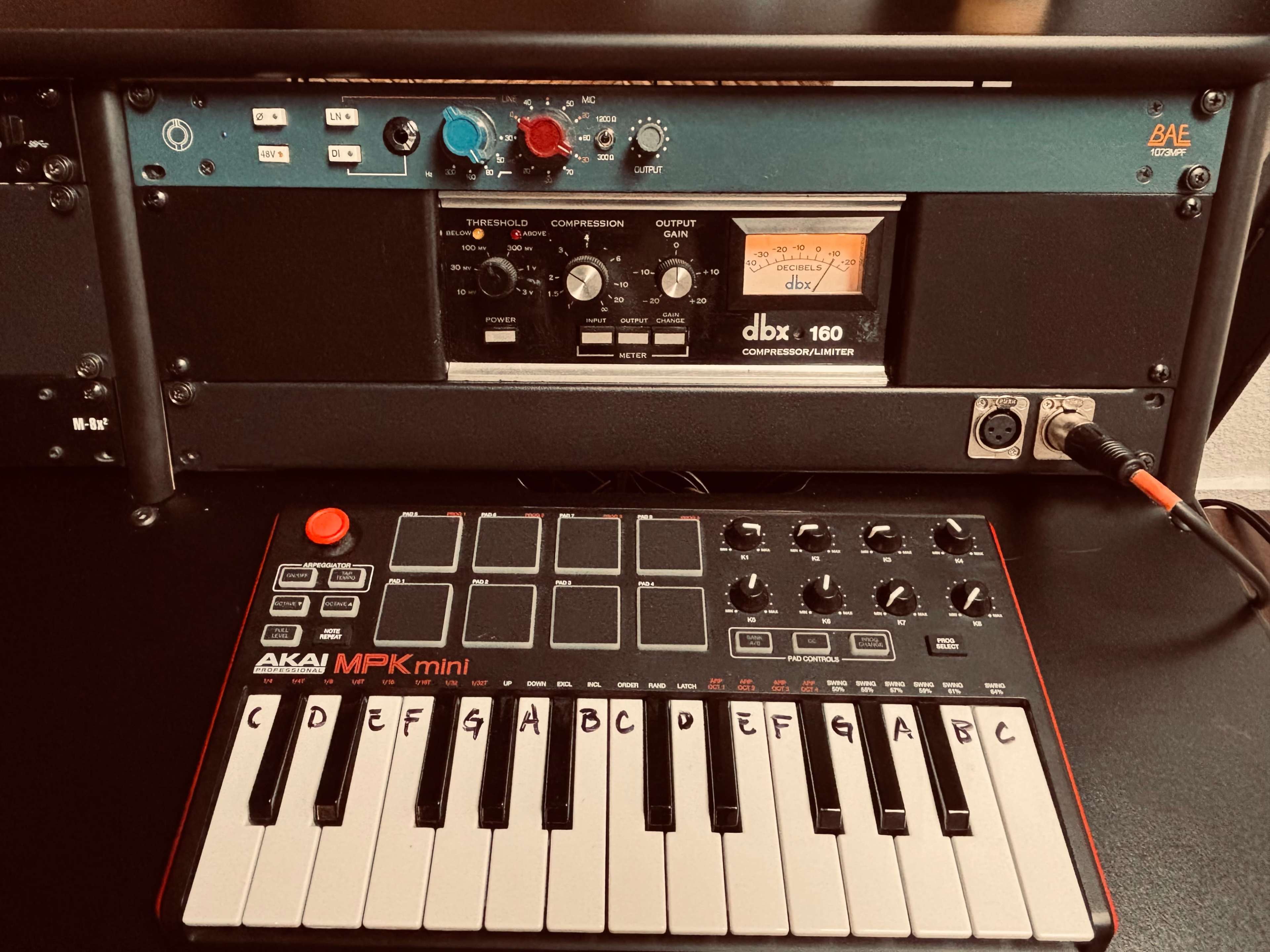 The image shows a close-up view of an audio setup that includes a DBA compression unit and an AKAI MPK mini keyboard controller.