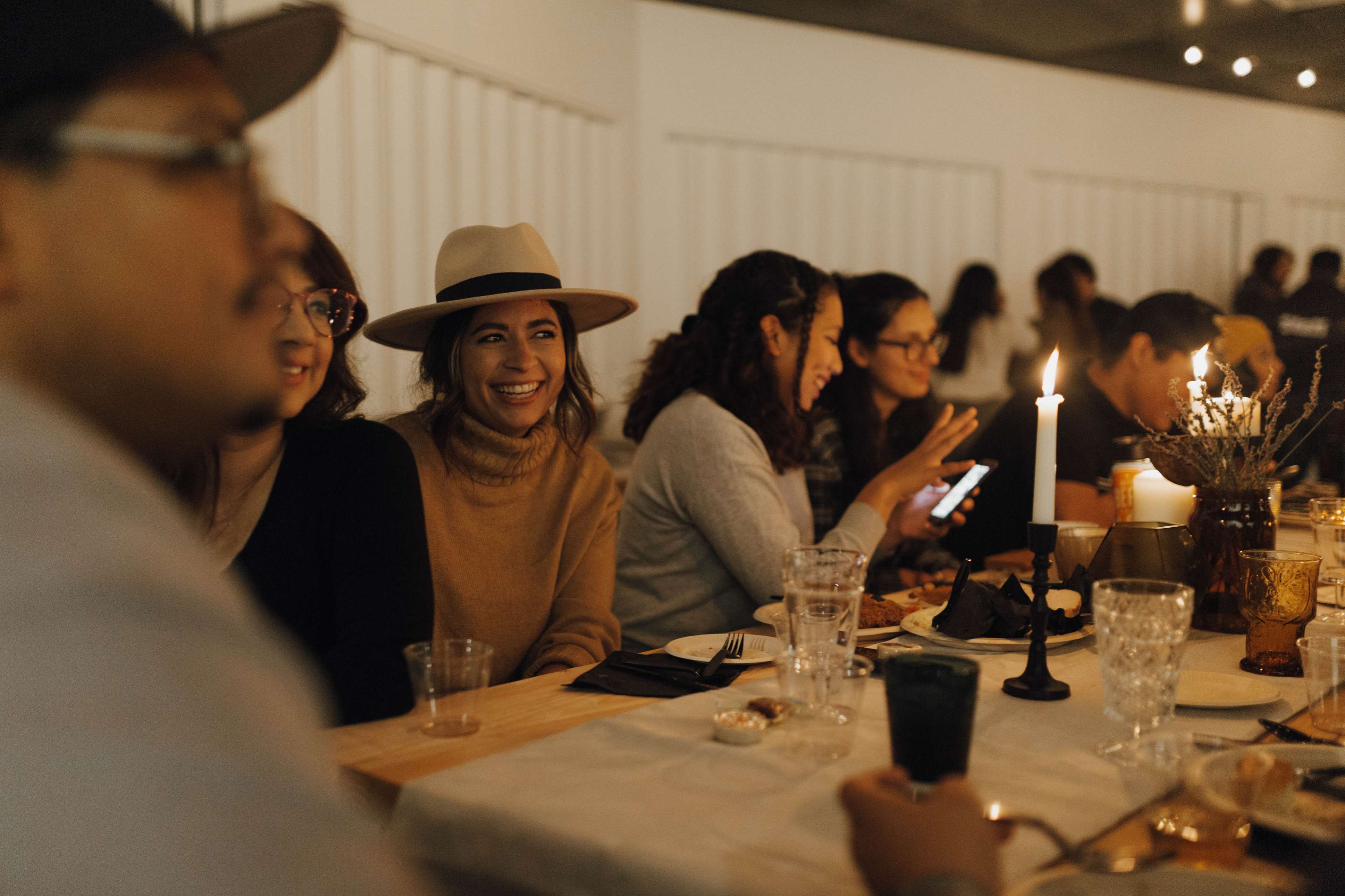 A group of people gathers around a long table adorned with candles and glasses, sharing smiles and conversations.