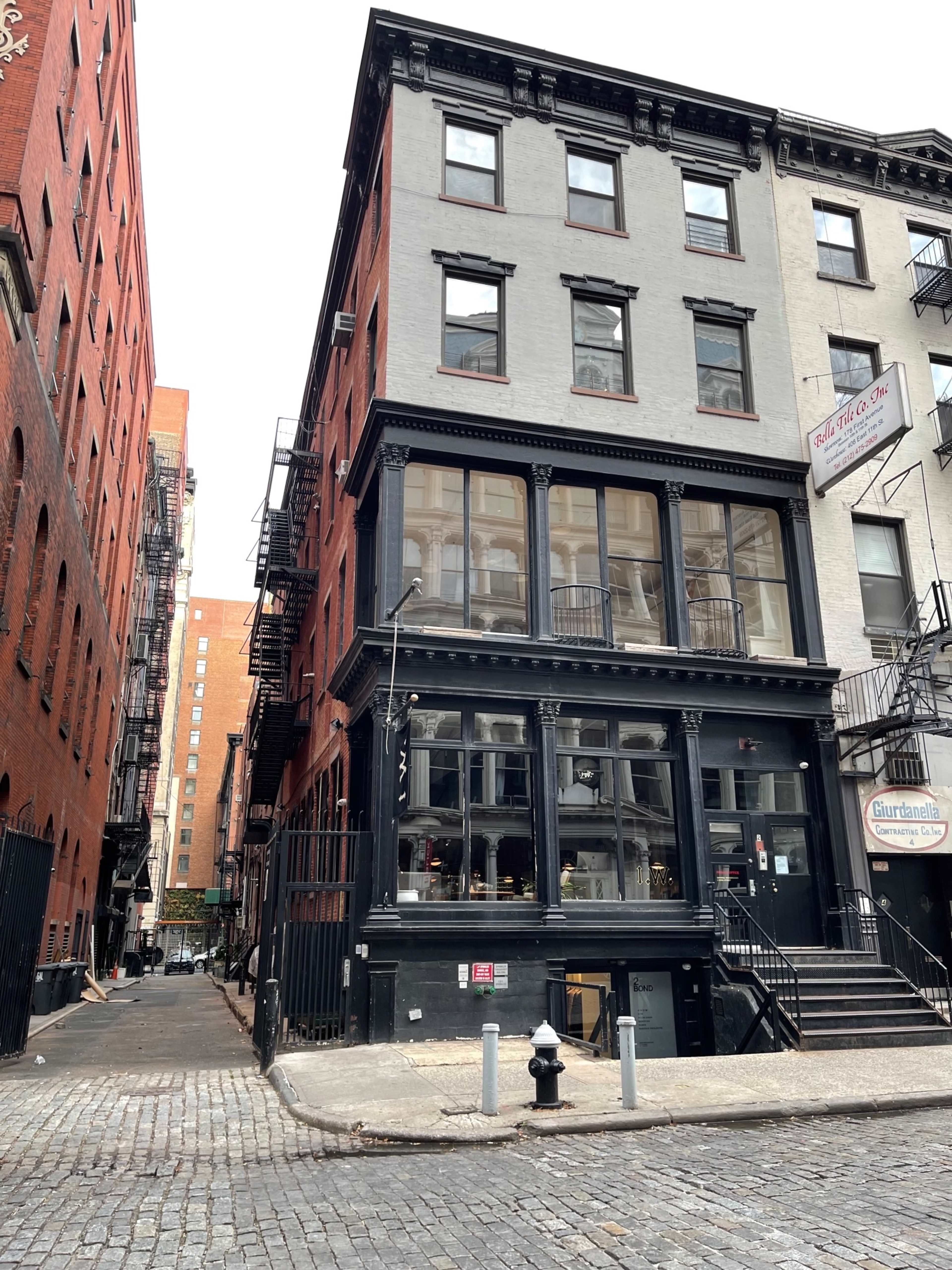 A narrow cobblestone street lined with brick buildings, featuring a three-story black and gray building with large windows on one side.