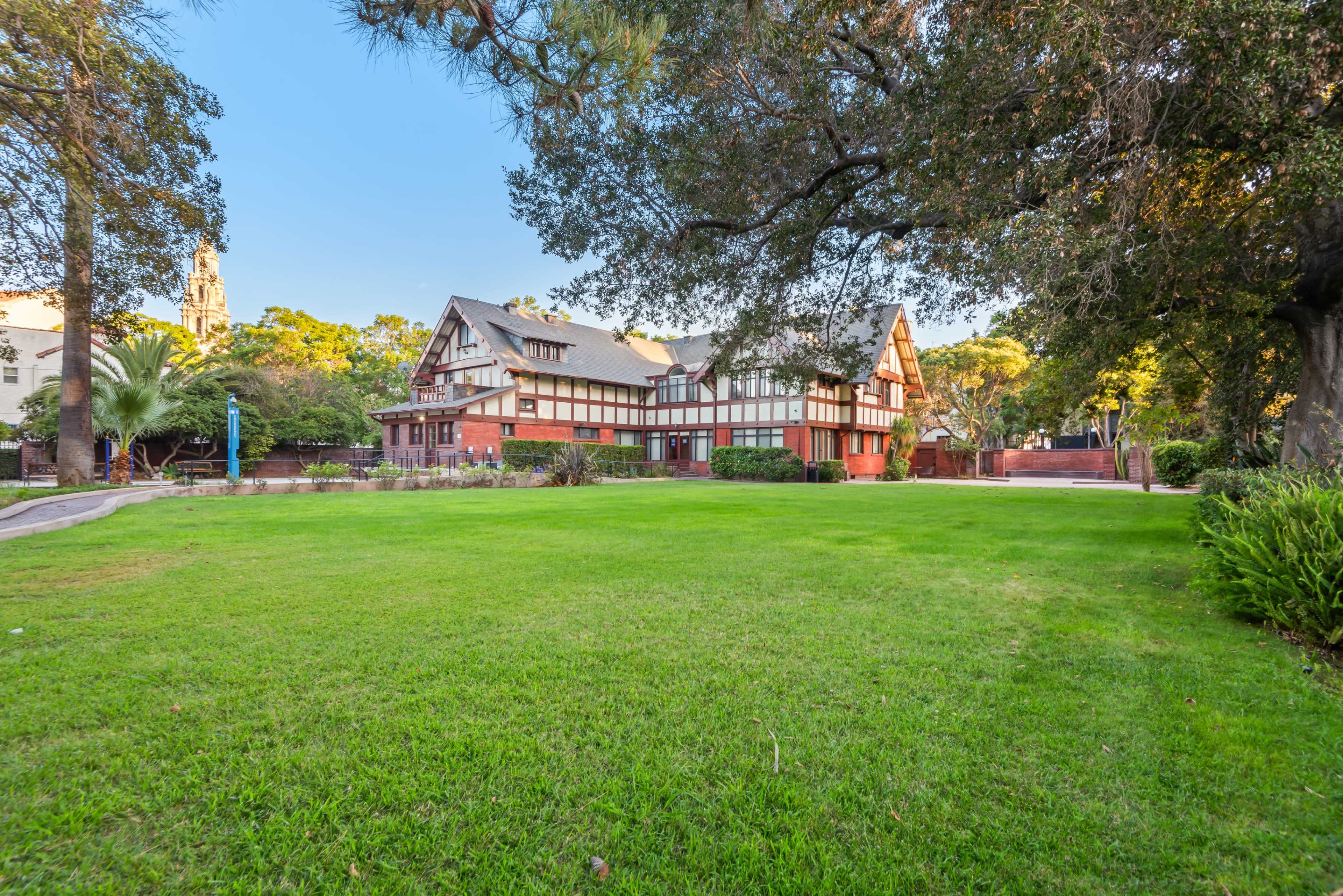 The image shows a large, historic brick building with a grassy lawn and trees surrounding it.