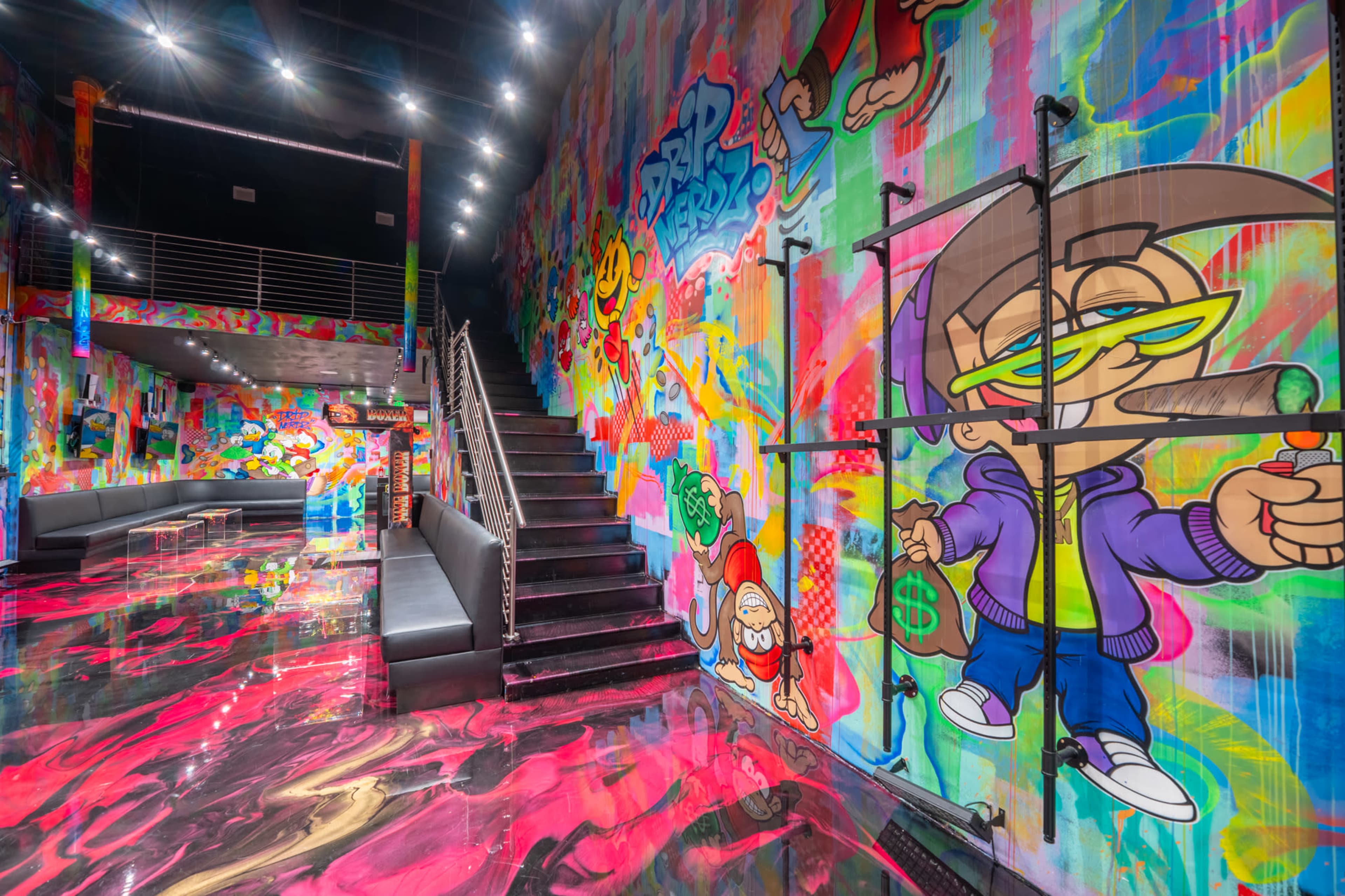 The image depicts a vibrant, graffiti-covered interior space featuring colorful murals on the walls and a staircase leading to an upper level.