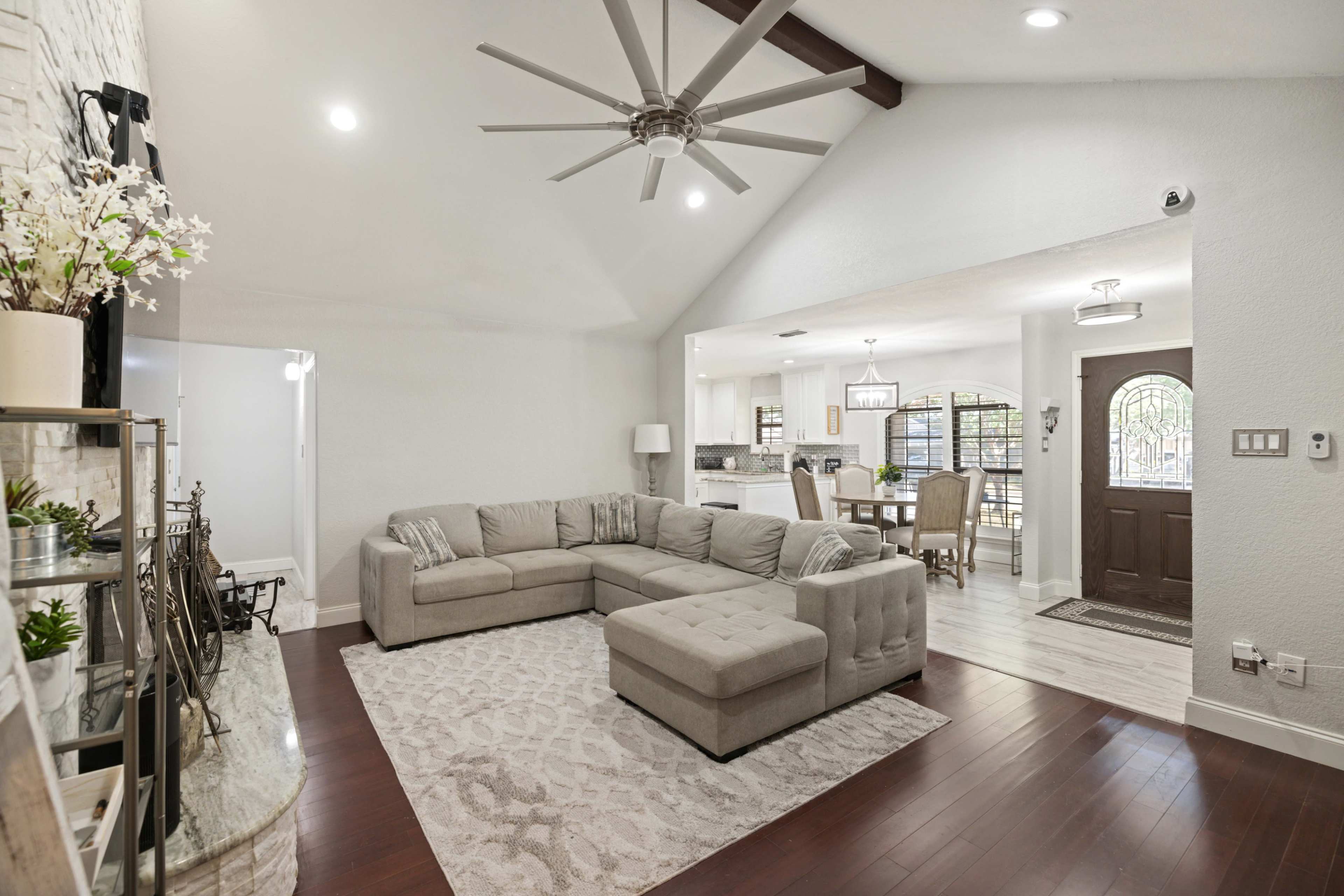 The living room features a large sectional sofa, a circular area rug, and a modern ceiling fan, with views into a dining area and entryway beyond.