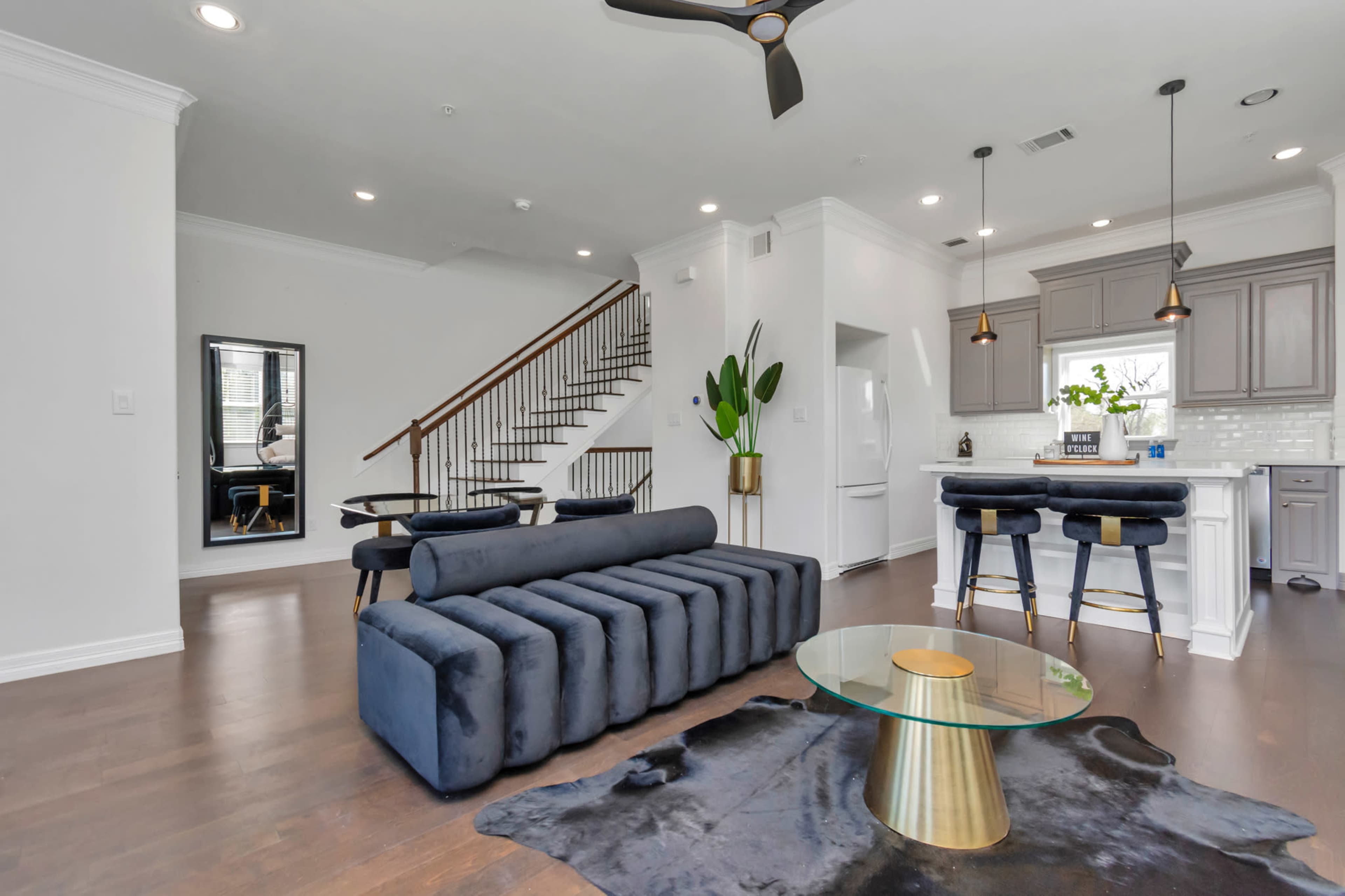 A modern living space featuring a sectional sofa, a glass coffee table on a rug, and a staircase leading to an upper level.