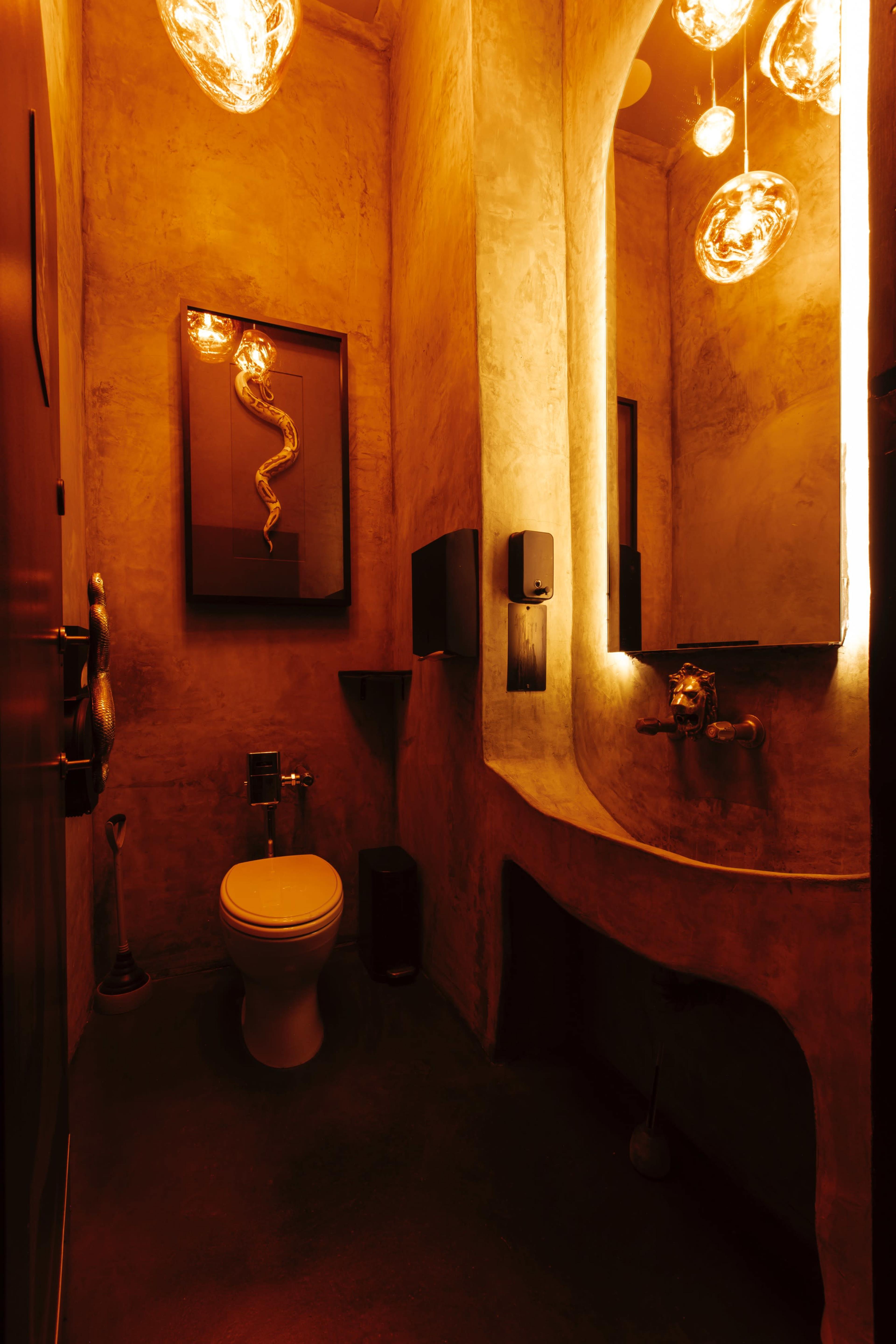 A dimly lit bathroom featuring a toilet, a curved sink, and decorative wall lighting.