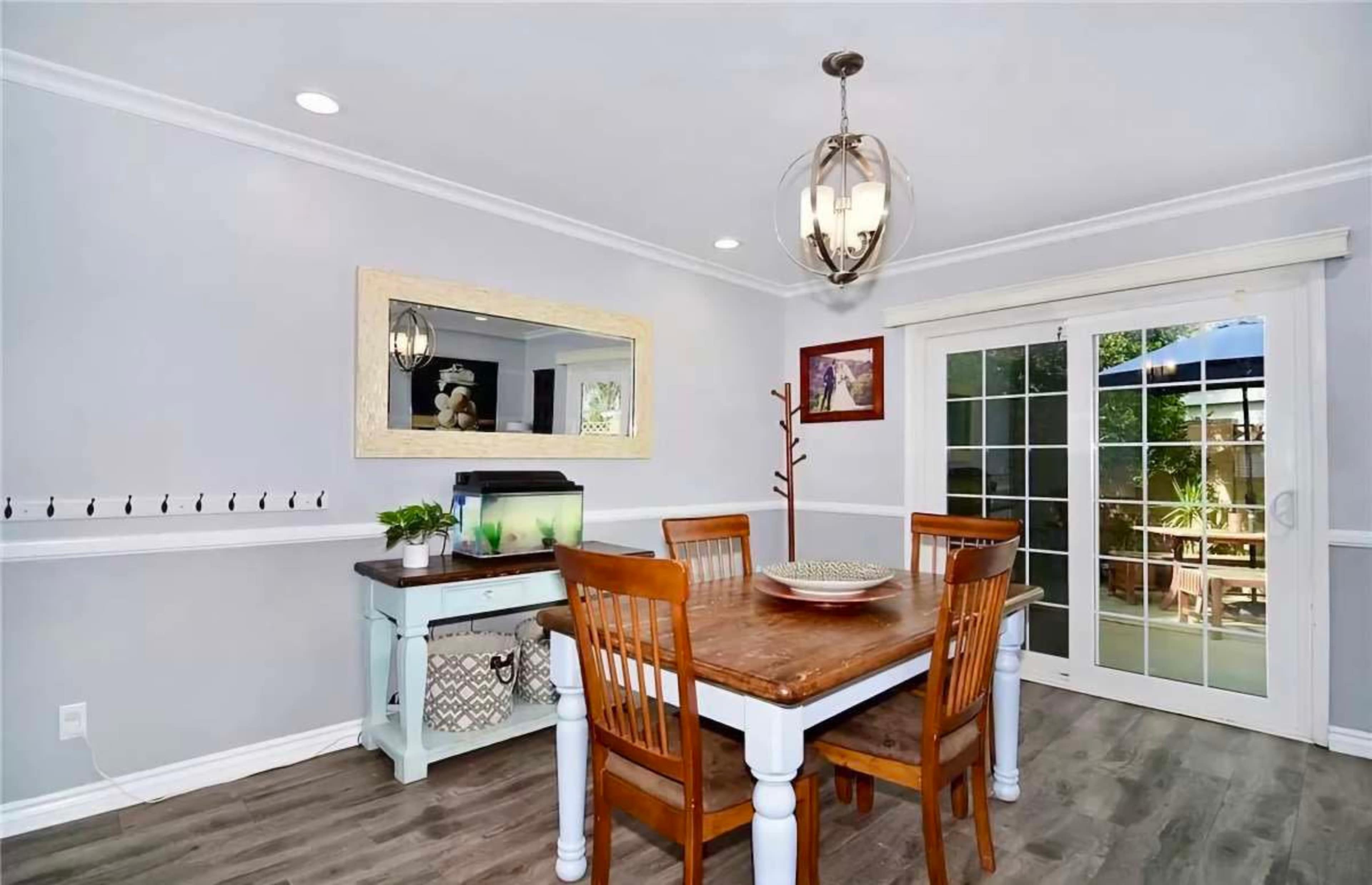 A dining area features a wooden table surrounded by four chairs, with a glass door leading to an outdoor space and an aquarium on a side table.