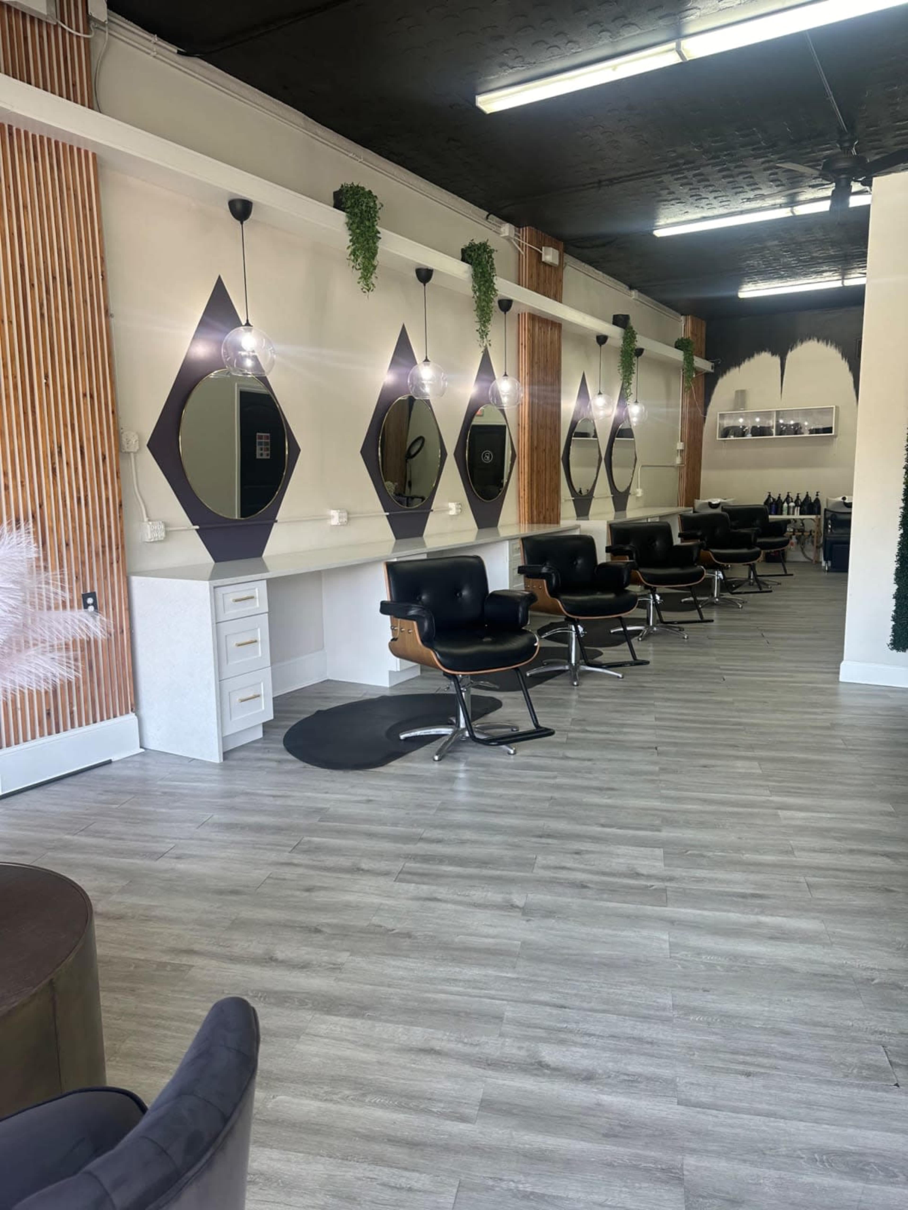 The image shows a modern hair salon with multiple styling stations featuring large mirrors and black chairs along a well-lit, minimalist interior.