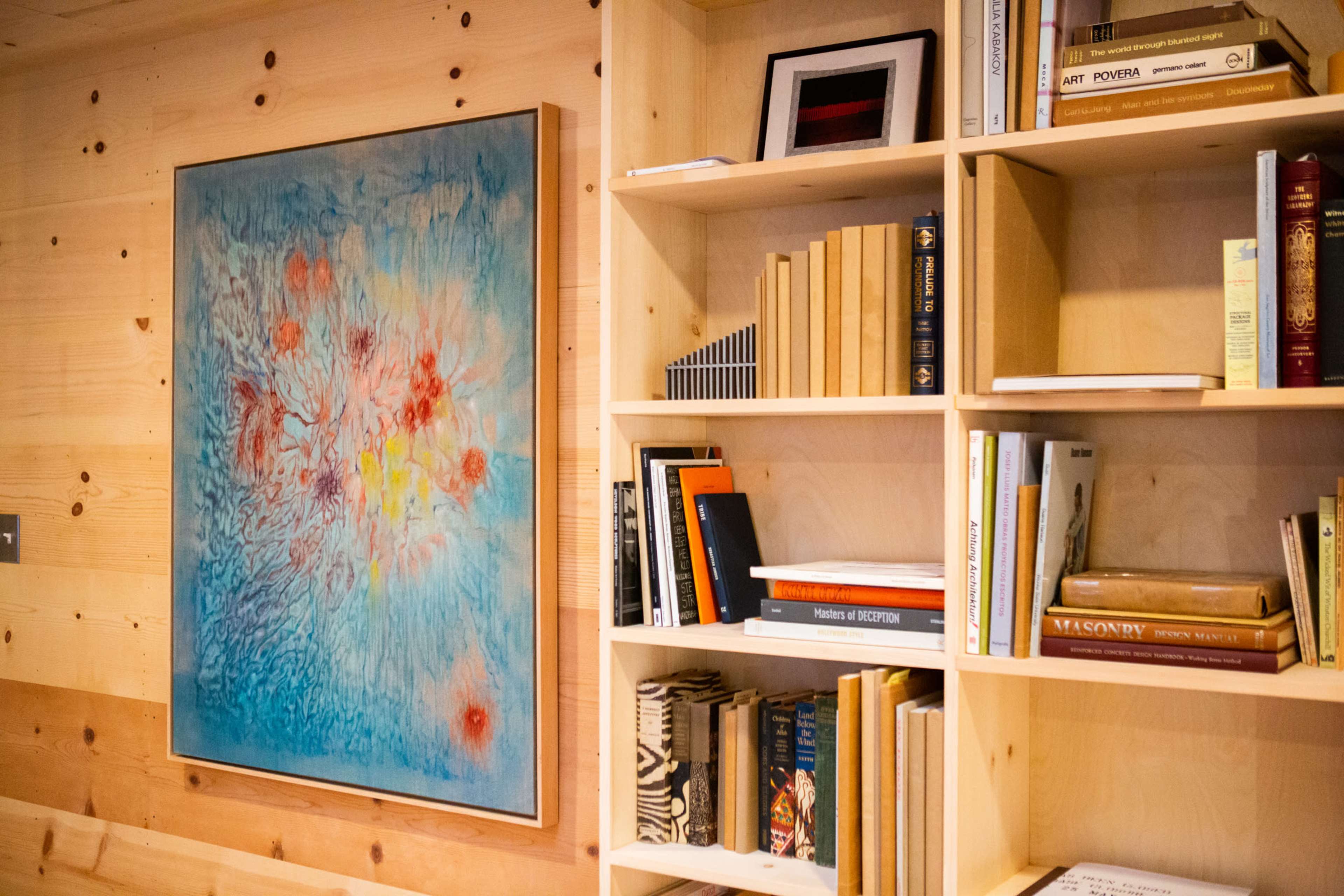 A wooden wall with a colorful abstract painting on the left and a bookshelf filled with various books on the right.