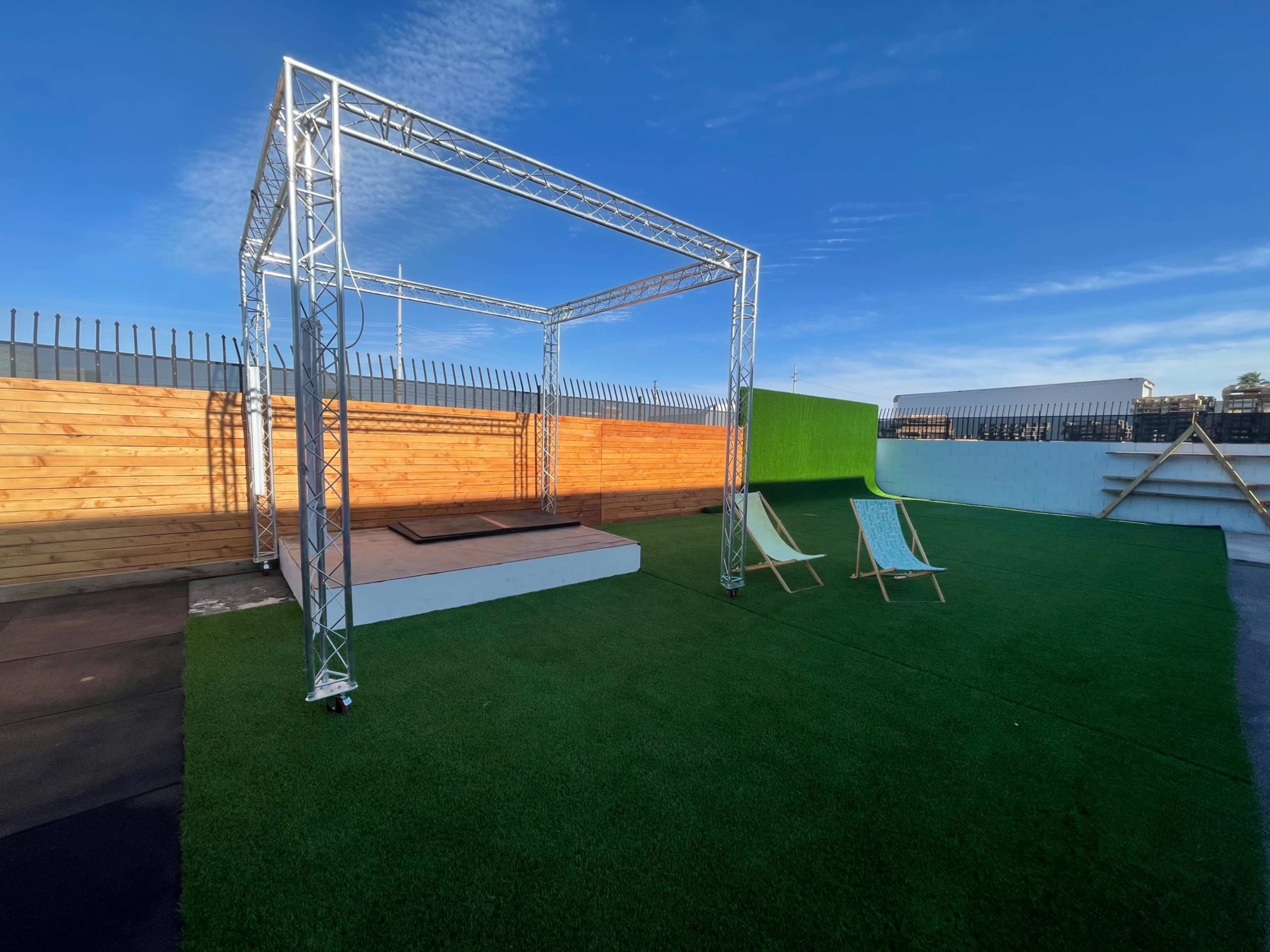 A rooftop space featuring a metal framework structure, a raised platform, and two deck chairs on artificial grass.