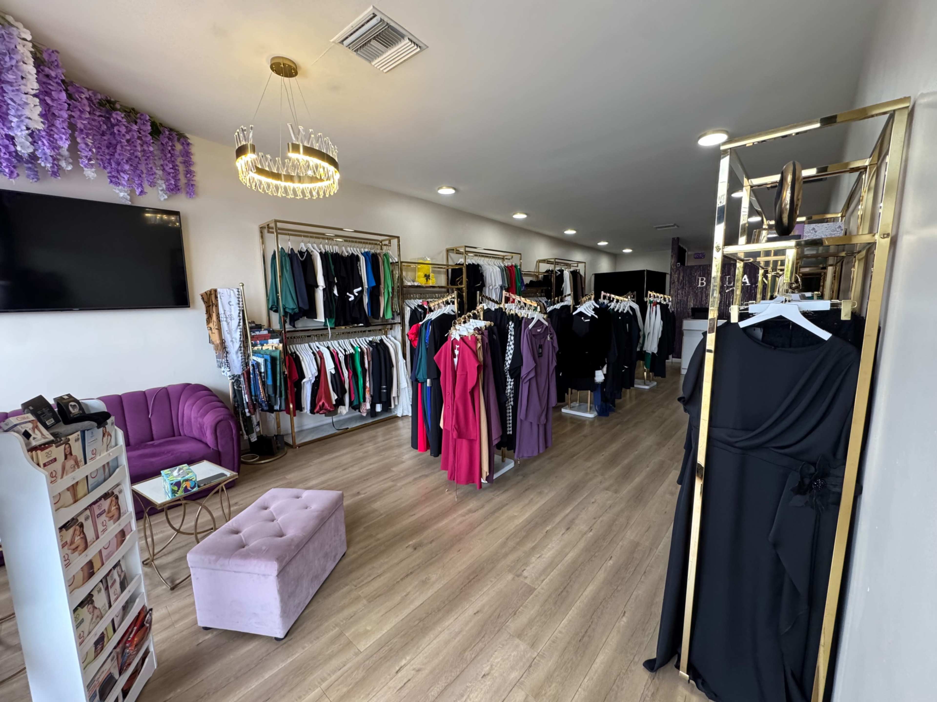 The image shows a clothing store interior with racks of colorful garments, a purple sofa, and a chandelier.