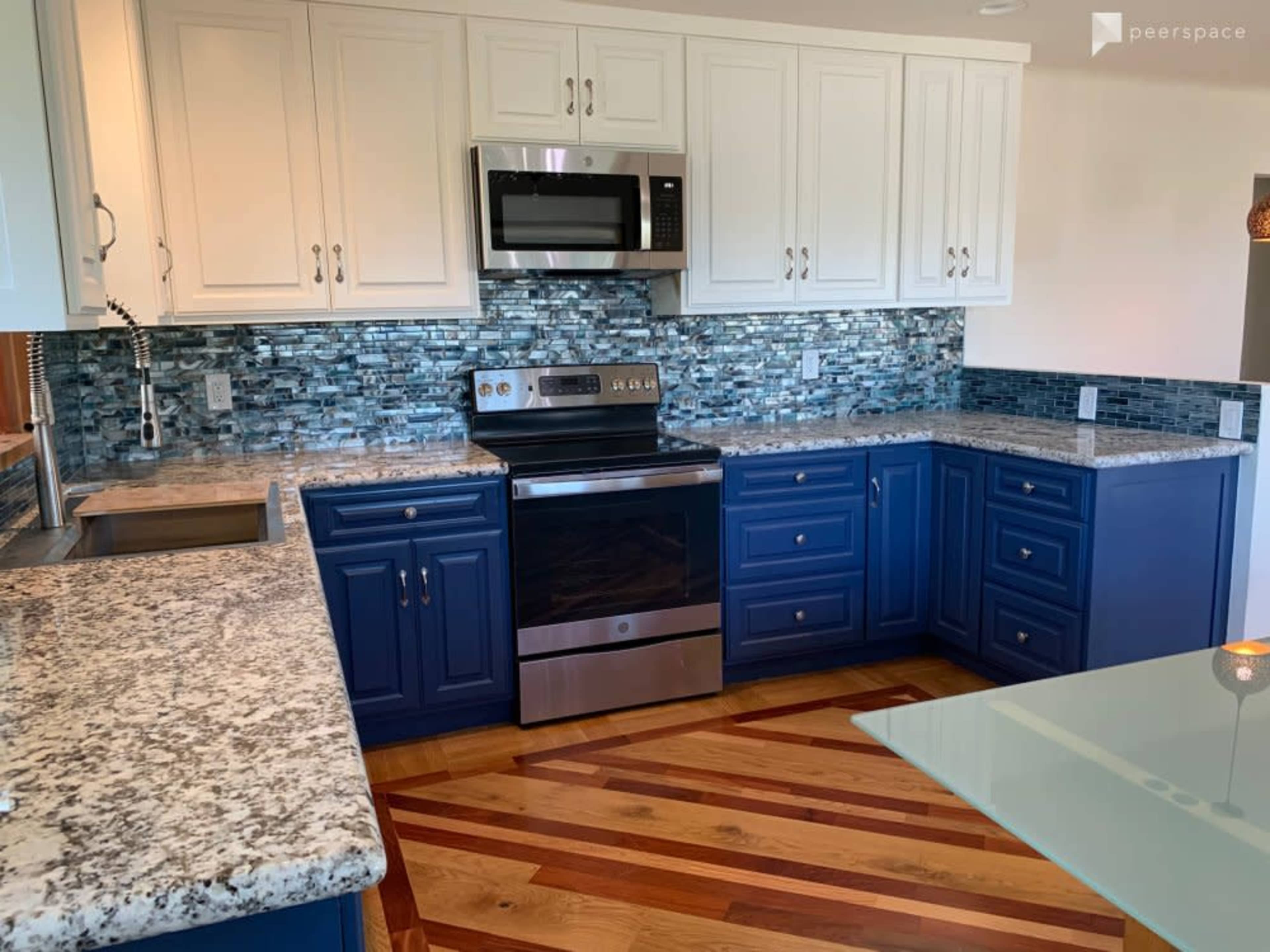 The image shows a modern kitchen with white upper cabinets, blue lower cabinets, granite countertops, and a stainless steel microwave and oven.