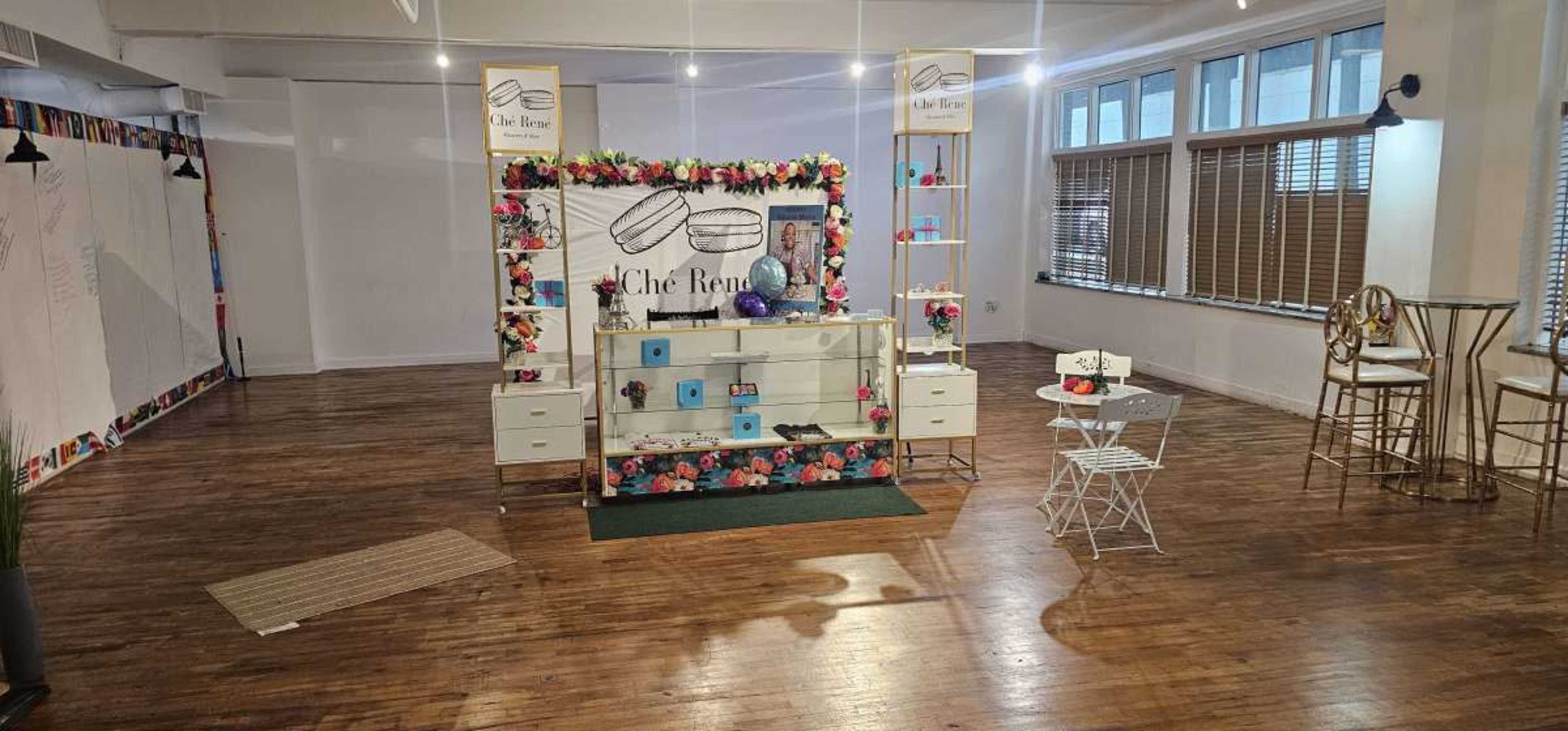 The image shows a decorated display area featuring a product showcase with floral accents and seating in a spacious, well-lit room.