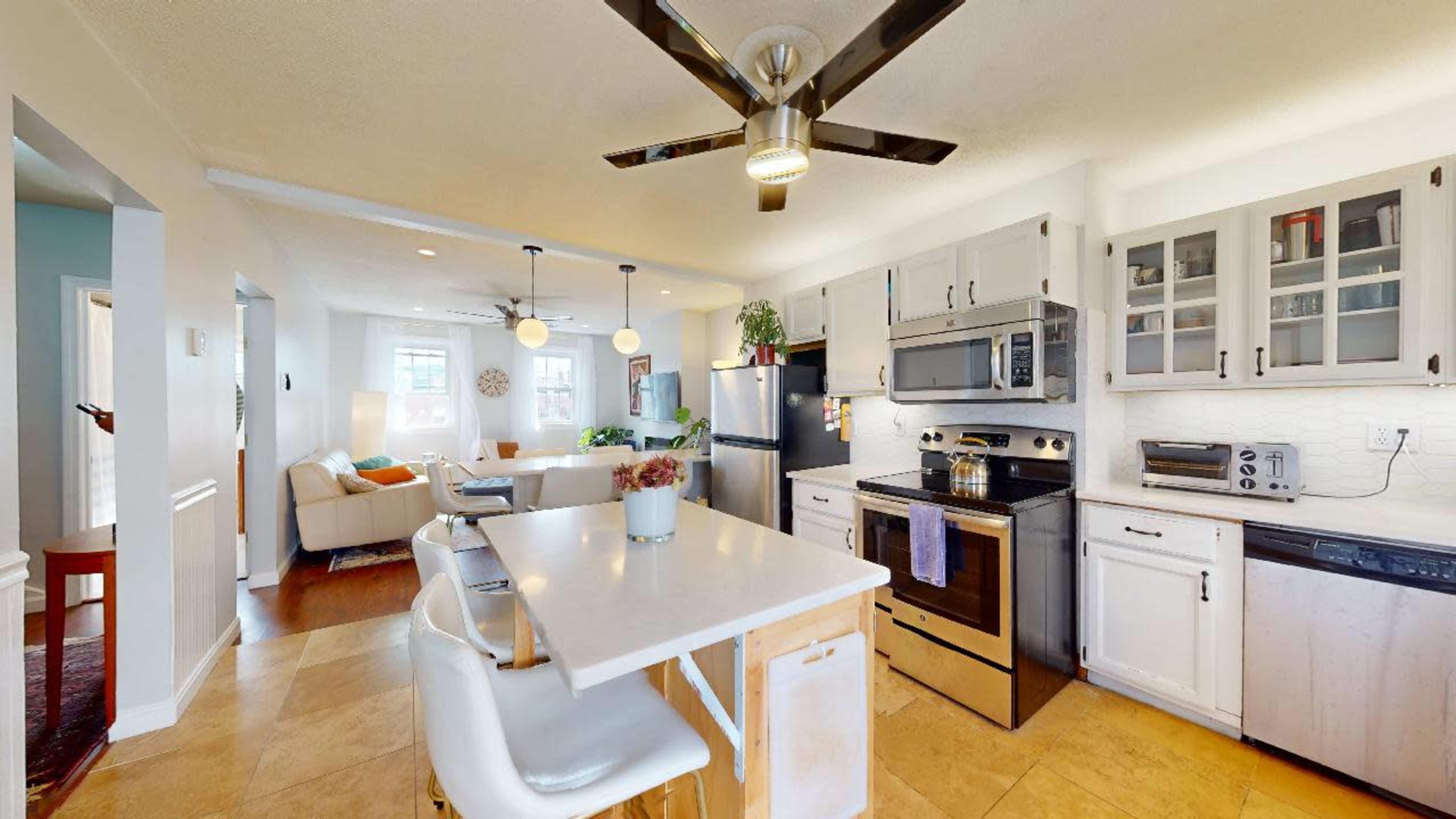The kitchen features a central island with seating, stainless steel appliances, and white cabinetry that opens to a living area.