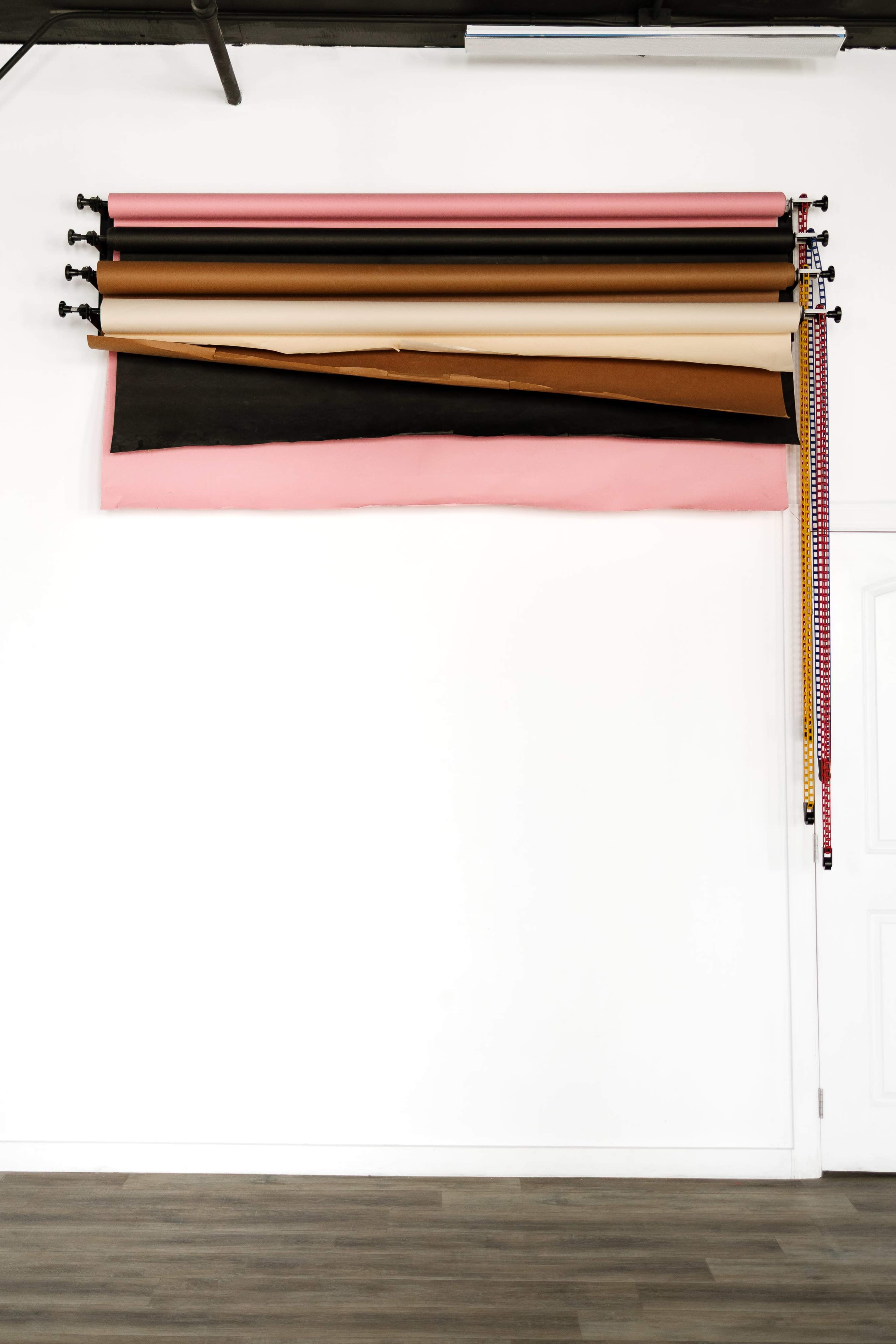 Several rolls of colored paper are mounted on a wall above a section of black fabric.