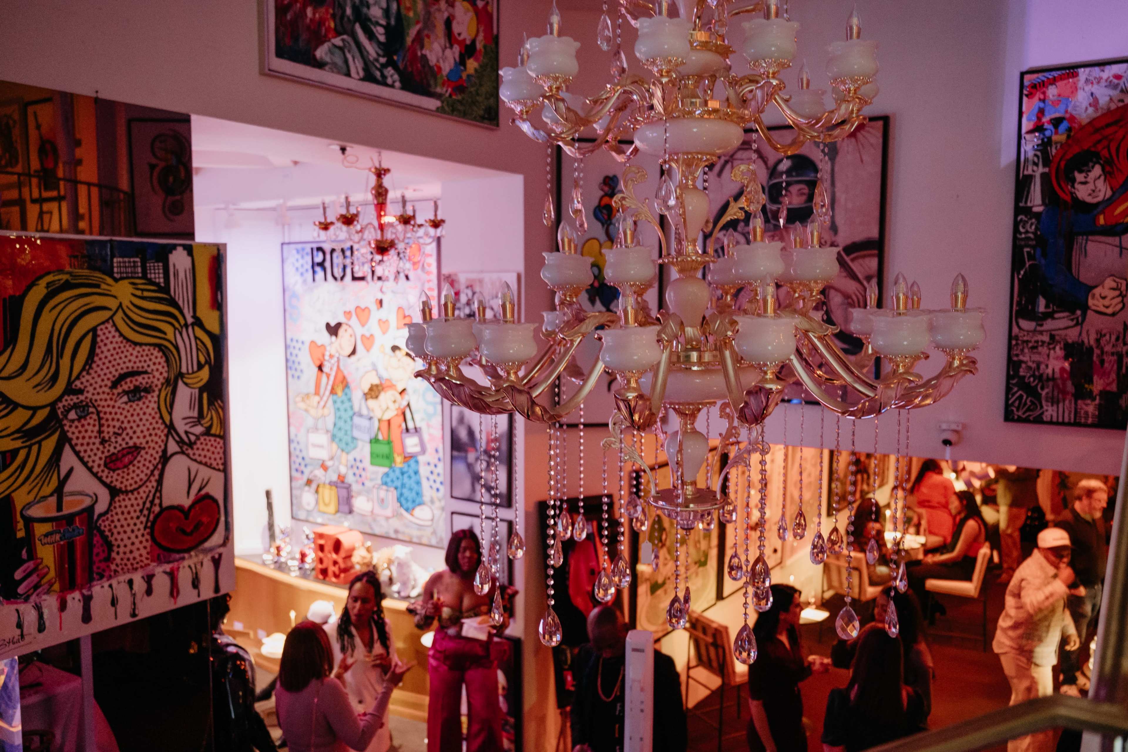 The image depicts an art gallery filled with colorful artworks and a glass chandelier, with attendees enjoying the vibrant atmosphere.