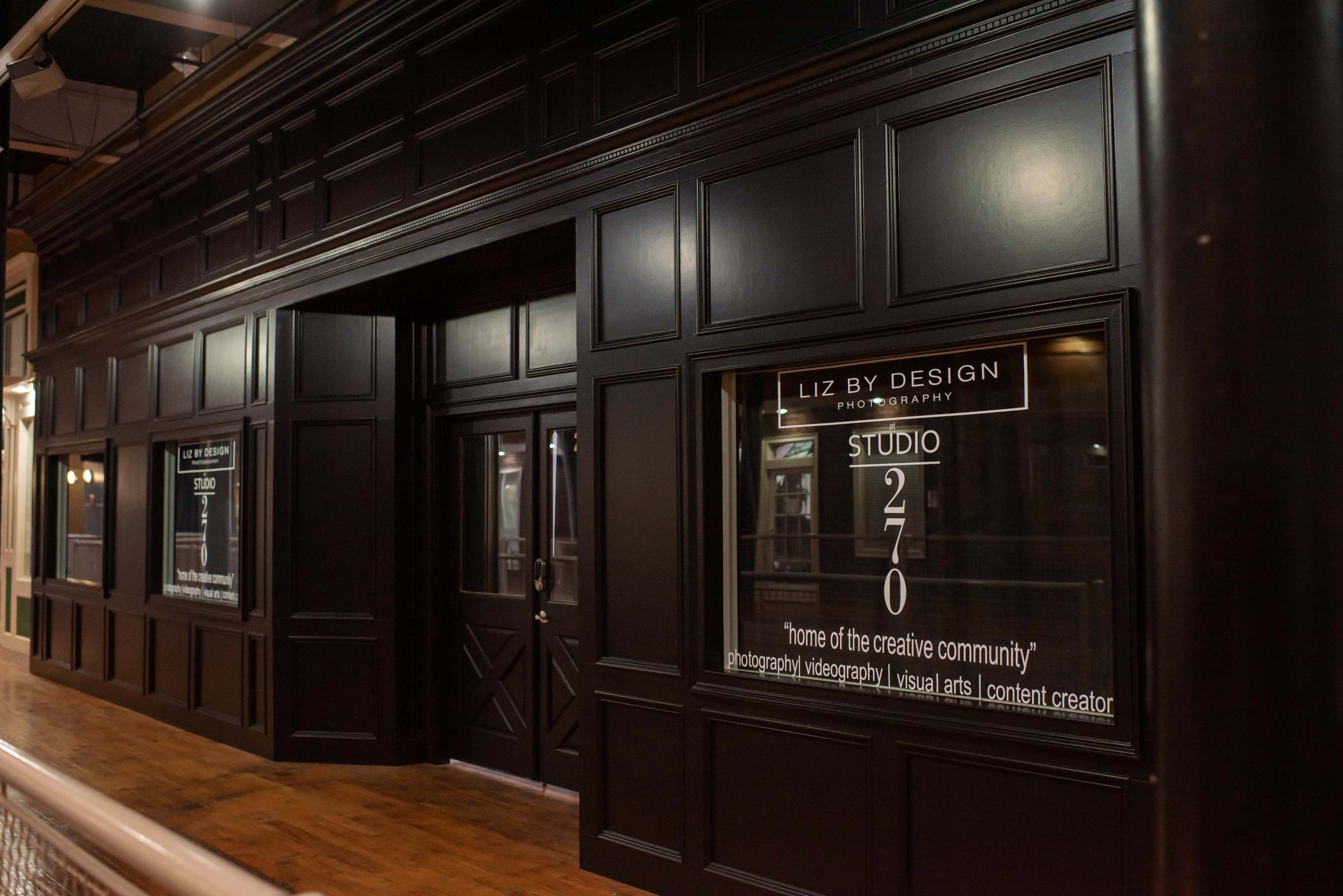 The image shows a storefront with a black exterior featuring large windows displaying the name "Liz By Design Photography" and information about studio services.