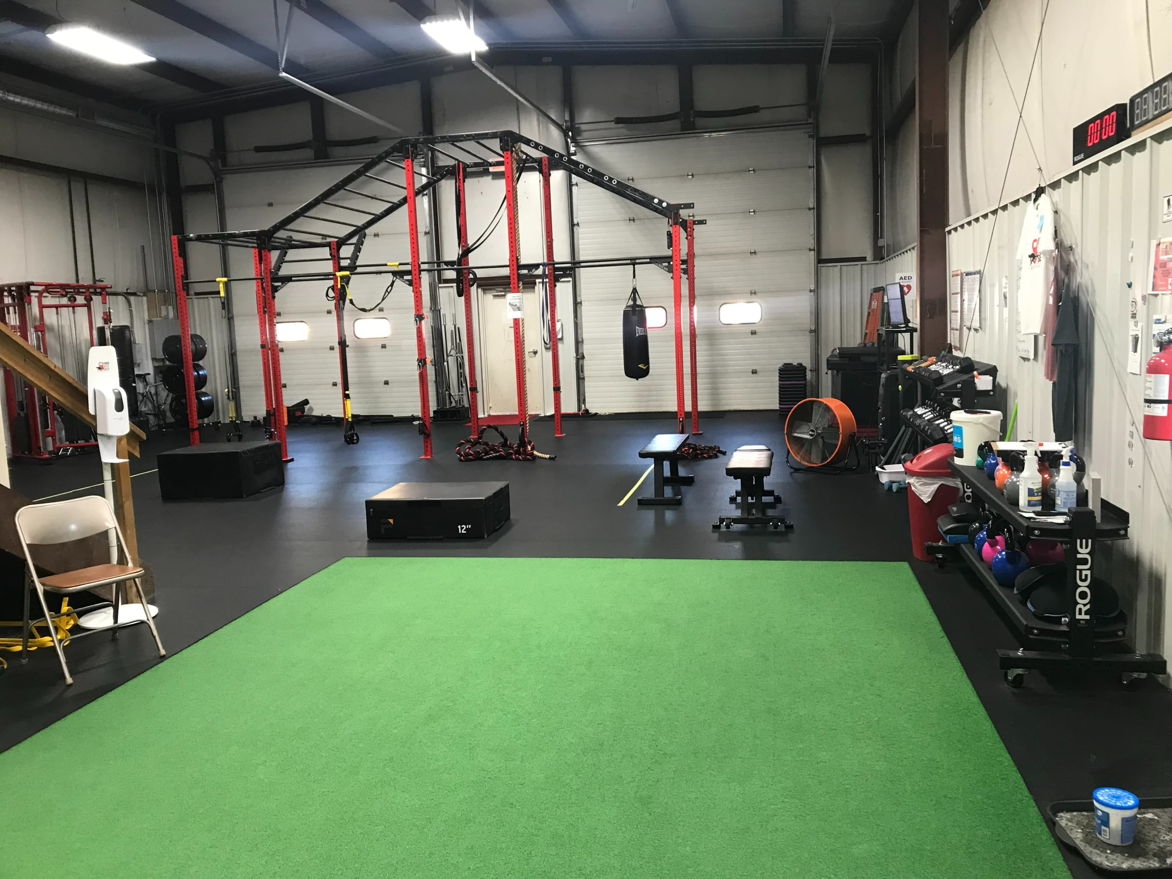 A spacious gym interior featuring exercise equipment, a green turf area, and various workout stations.