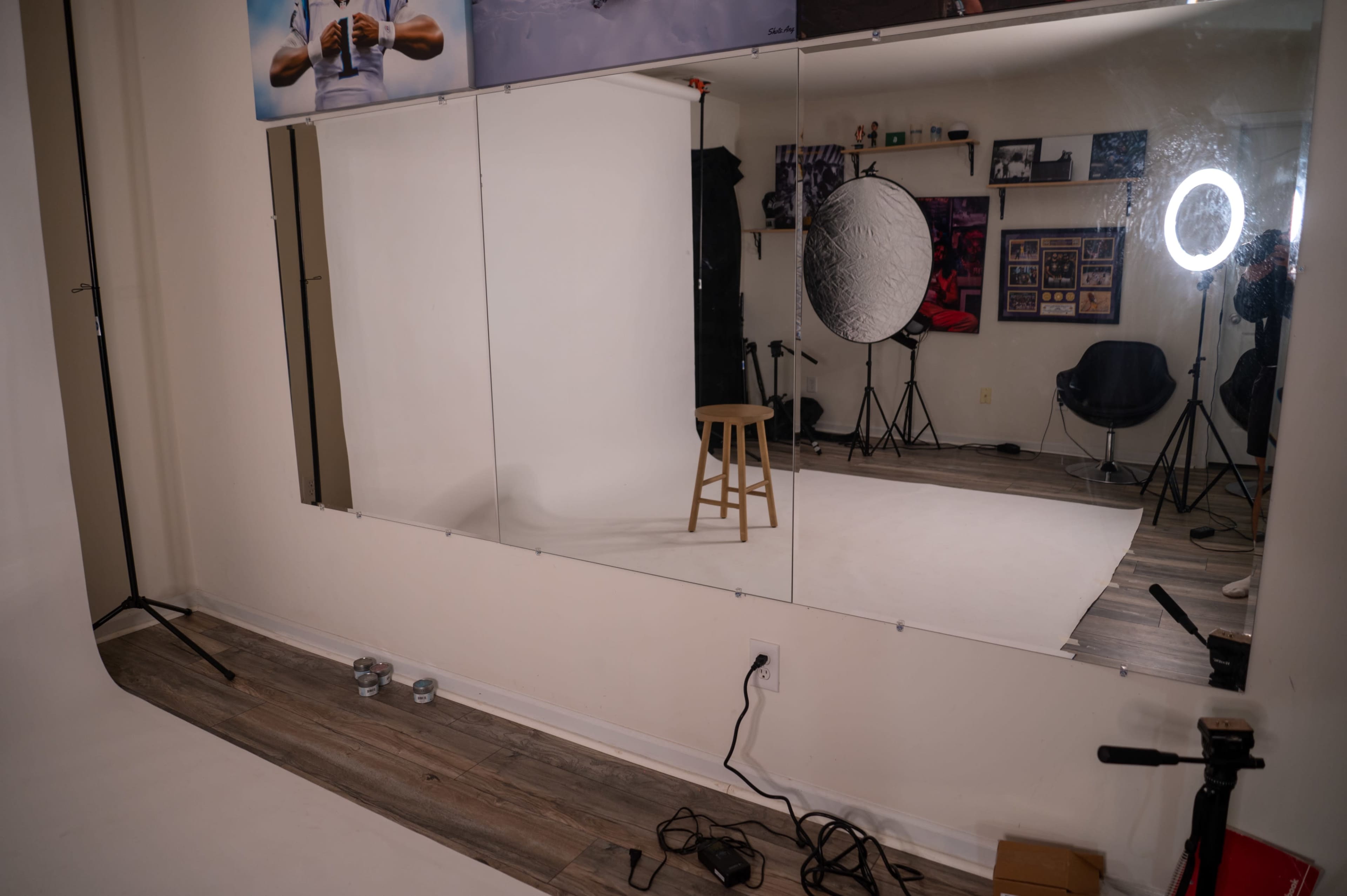 A photography studio with a mirror wall, a stool, and lighting equipment set up on a white backdrop.