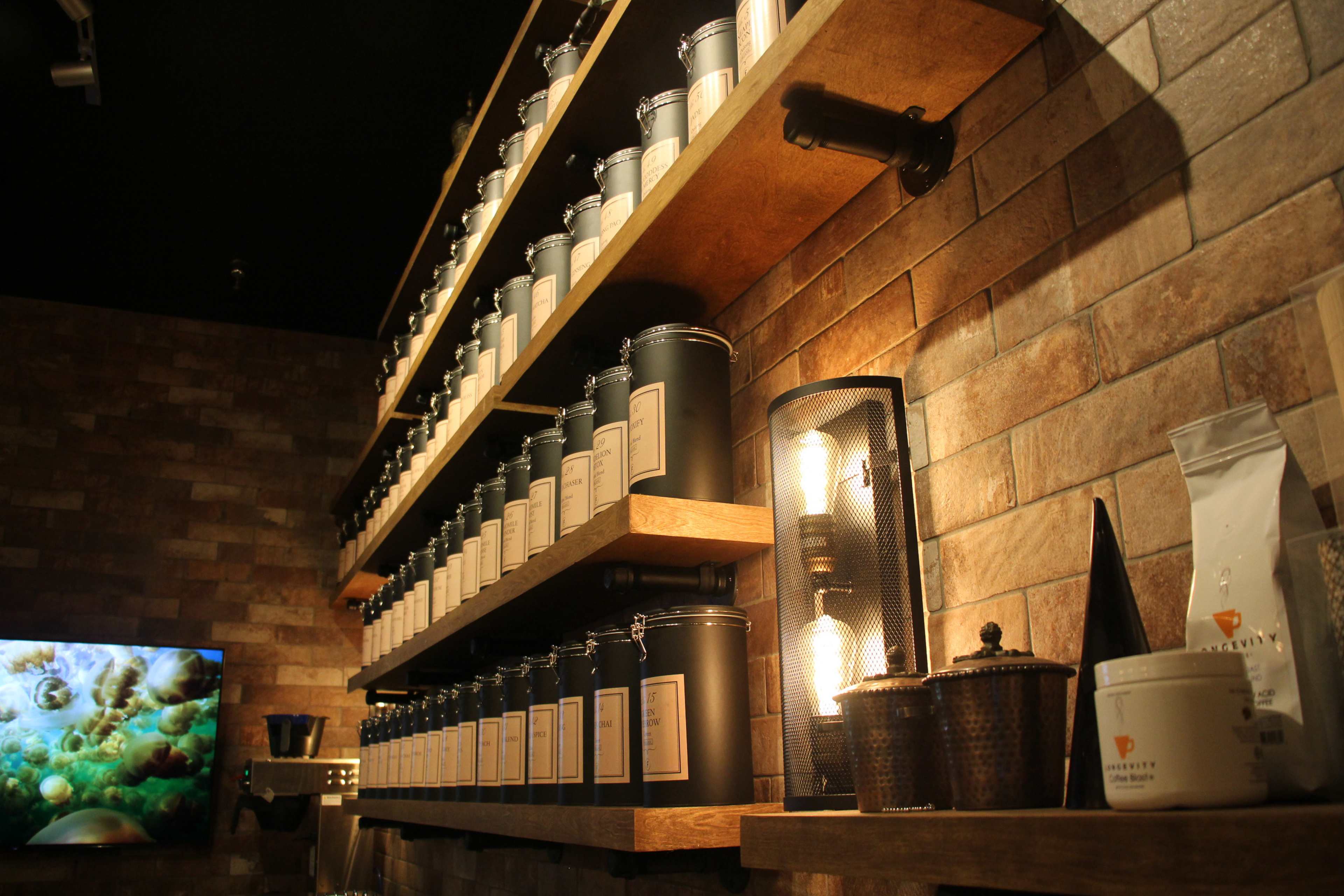 A wooden shelf displaying a row of black containers labeled with text, alongside a warm light source and a decorative metal lantern.