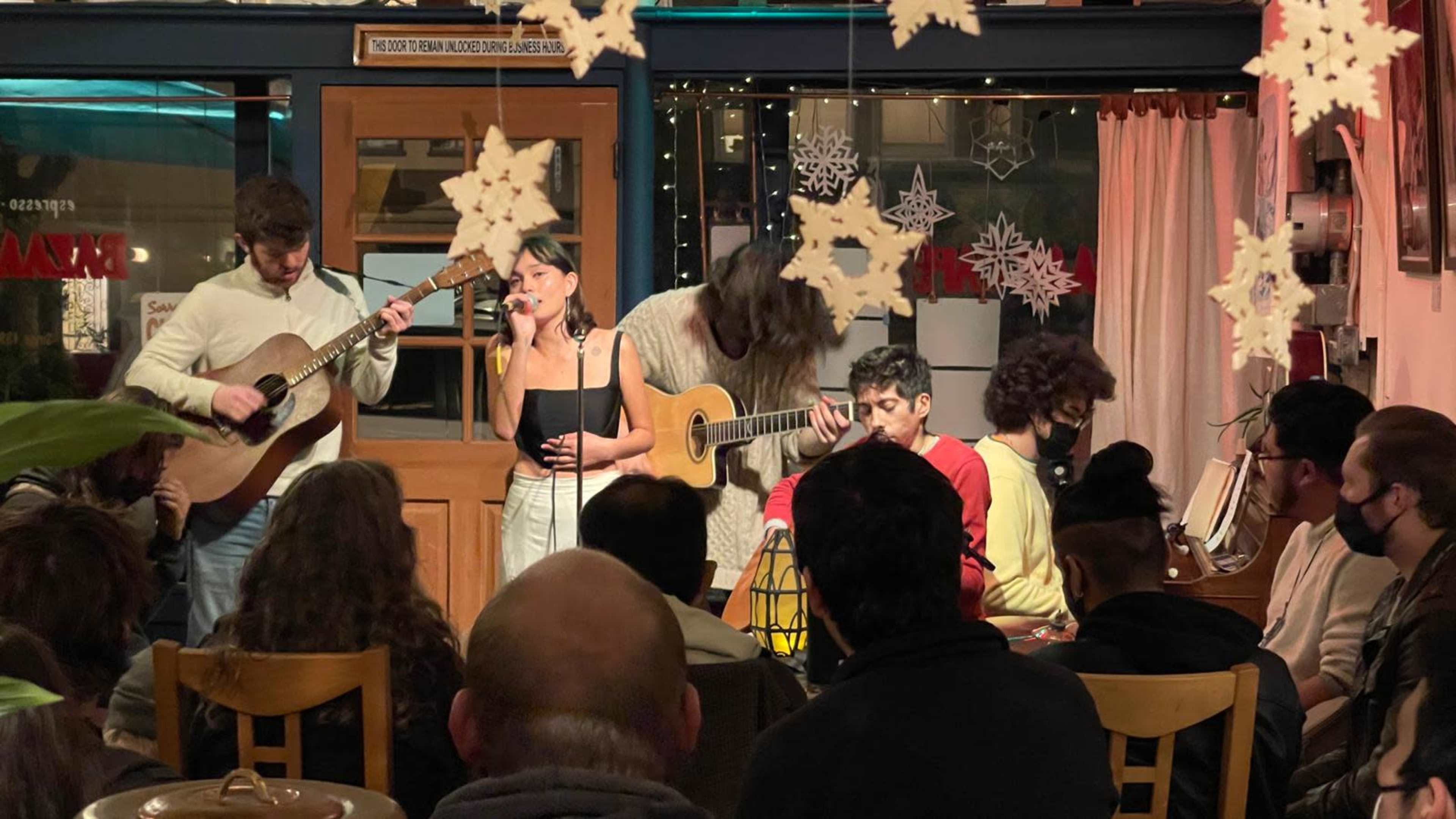 A group of musicians performs on stage in a cozy café while an audience watches attentively.