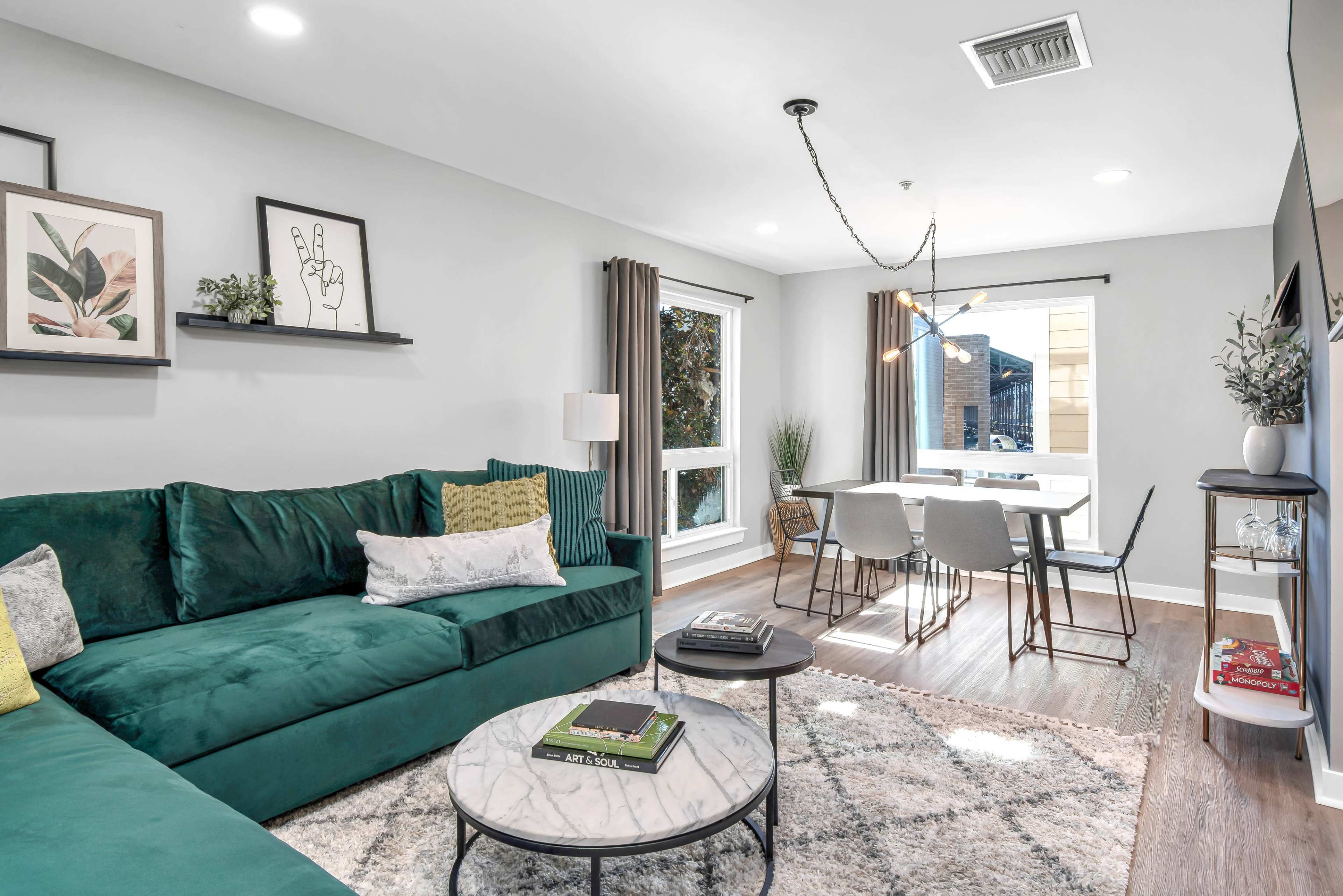 A modern living room with a green velvet sofa, a marble coffee table, and a dining area featuring a round table and dining chairs next to a window.