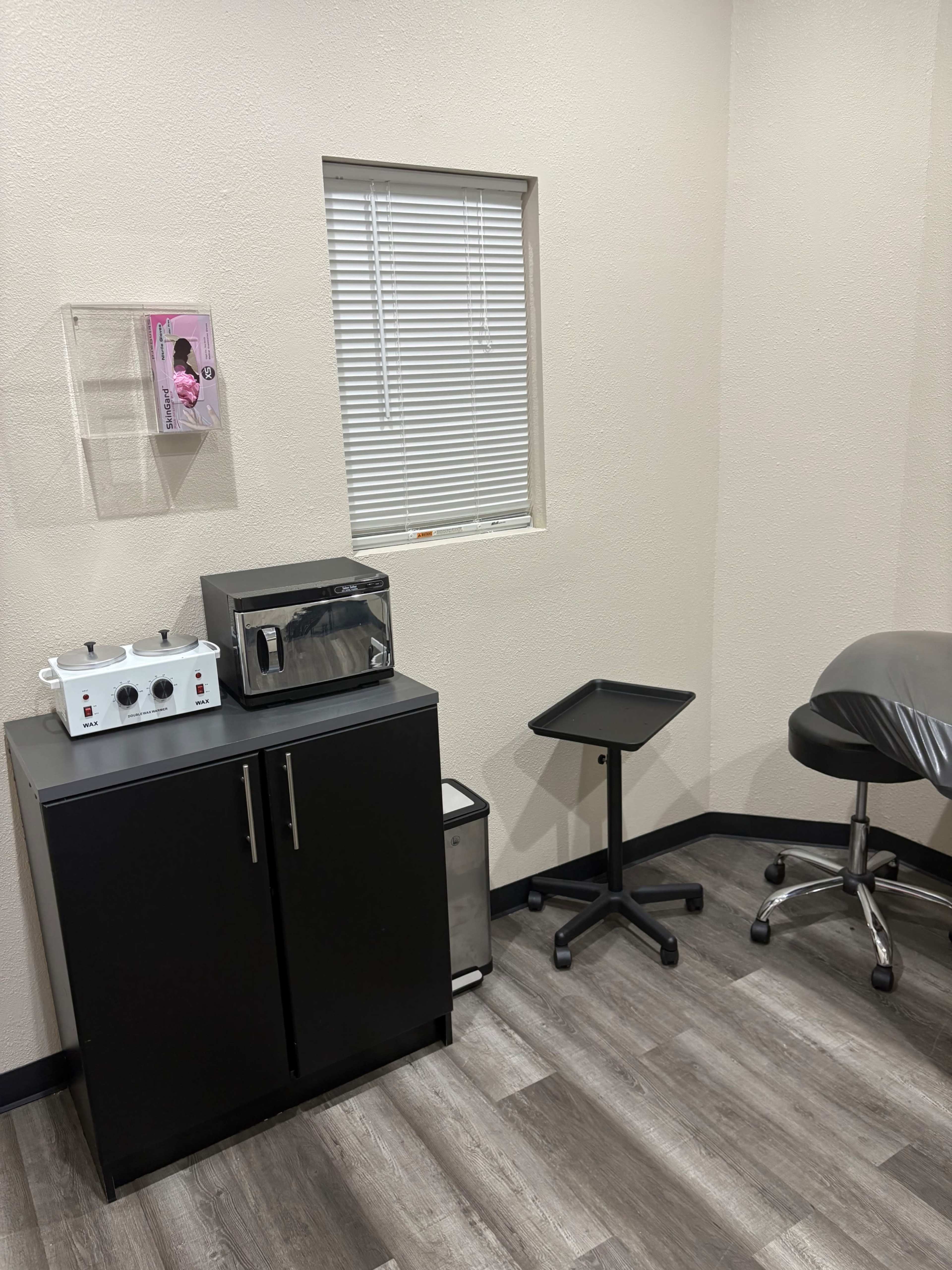 The image shows a small room with a microwave, a black cabinet, a movable tray, and a chair, all set against a light-colored wall with a window.