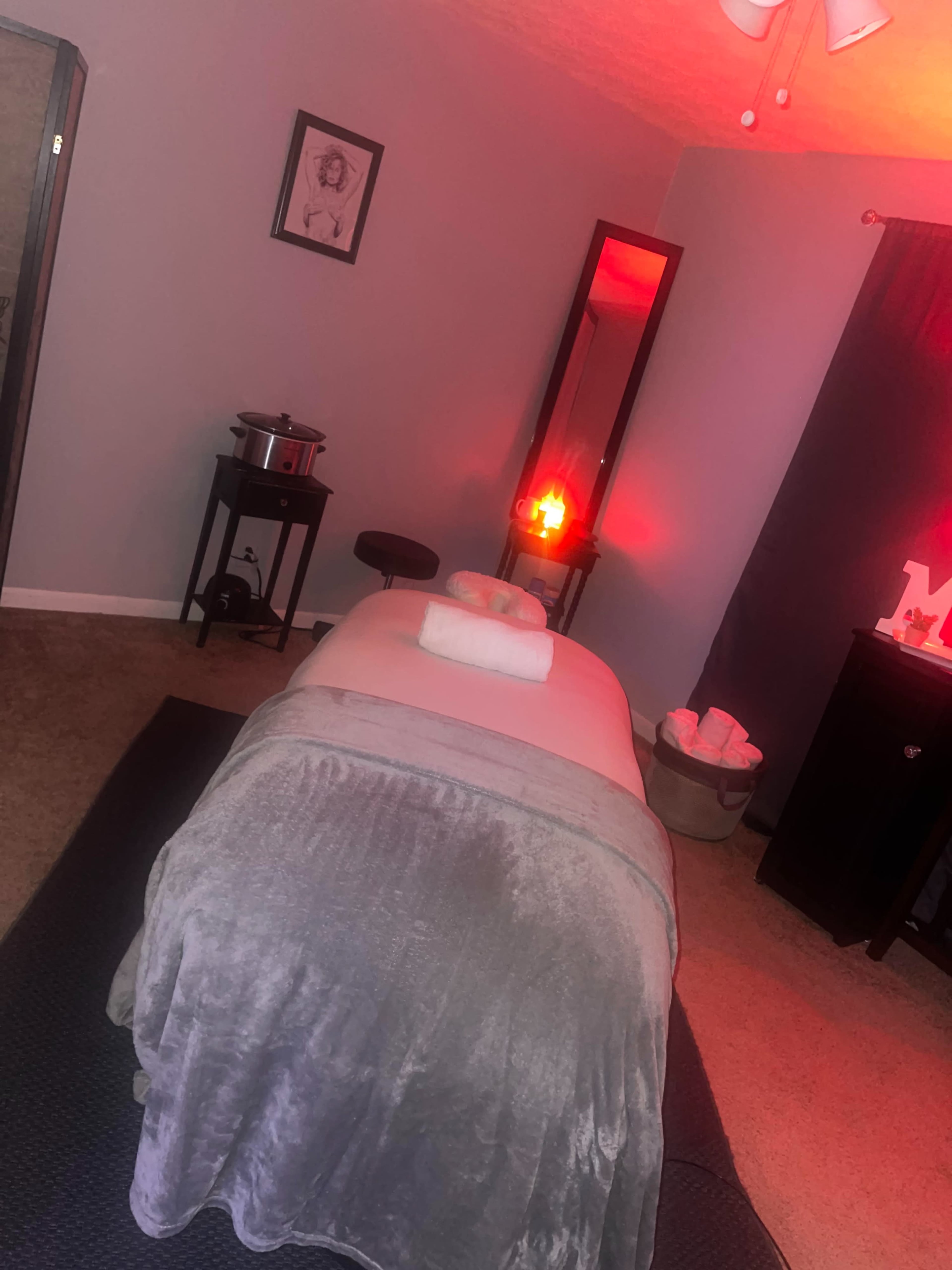 The image shows a serene massage room featuring a massage table with a towel, a mirror, a salt lamp, and a cozy seating area.