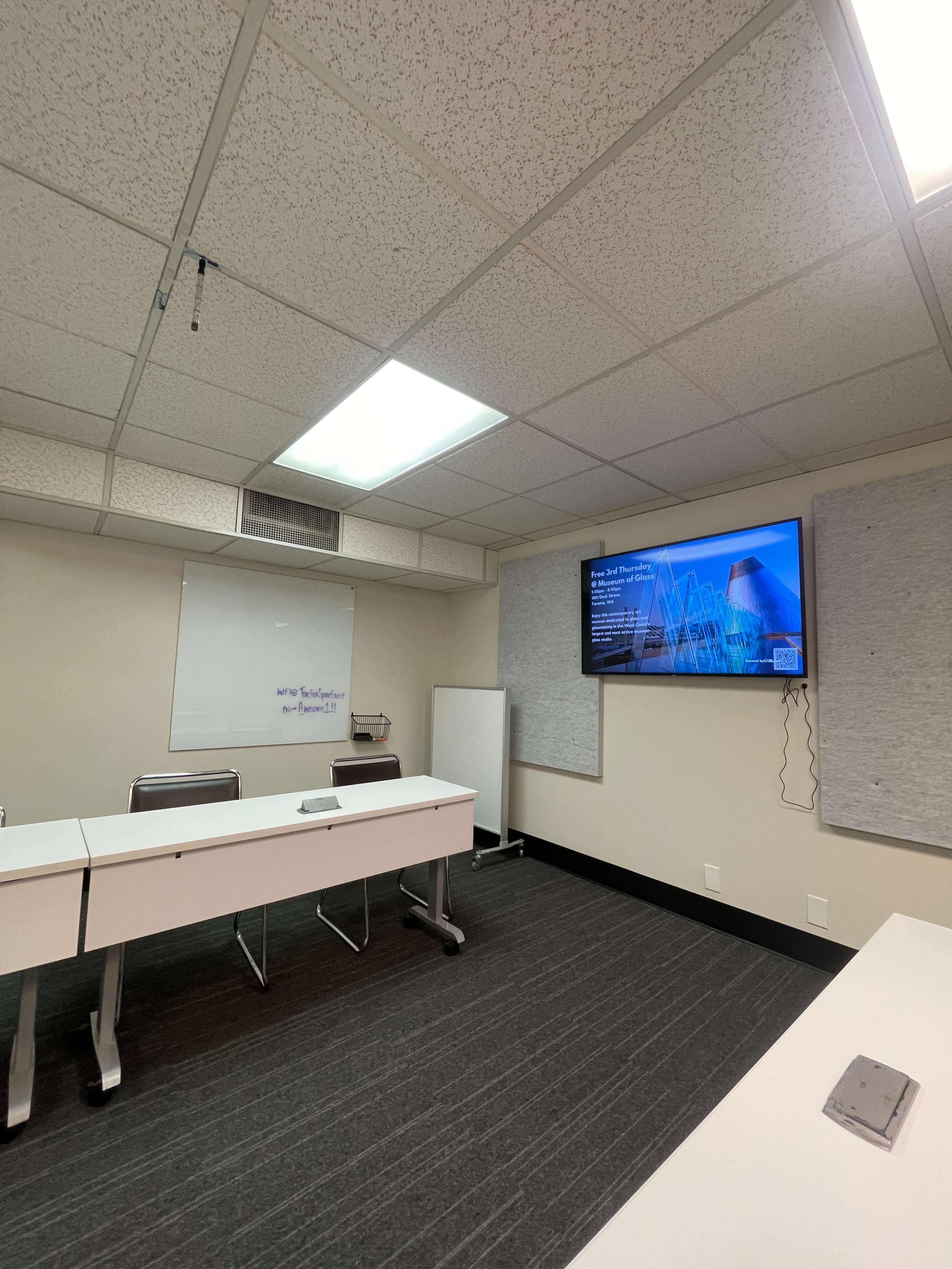 A conference room with a large screen displaying a presentation, whiteboards, and a long table with chairs.