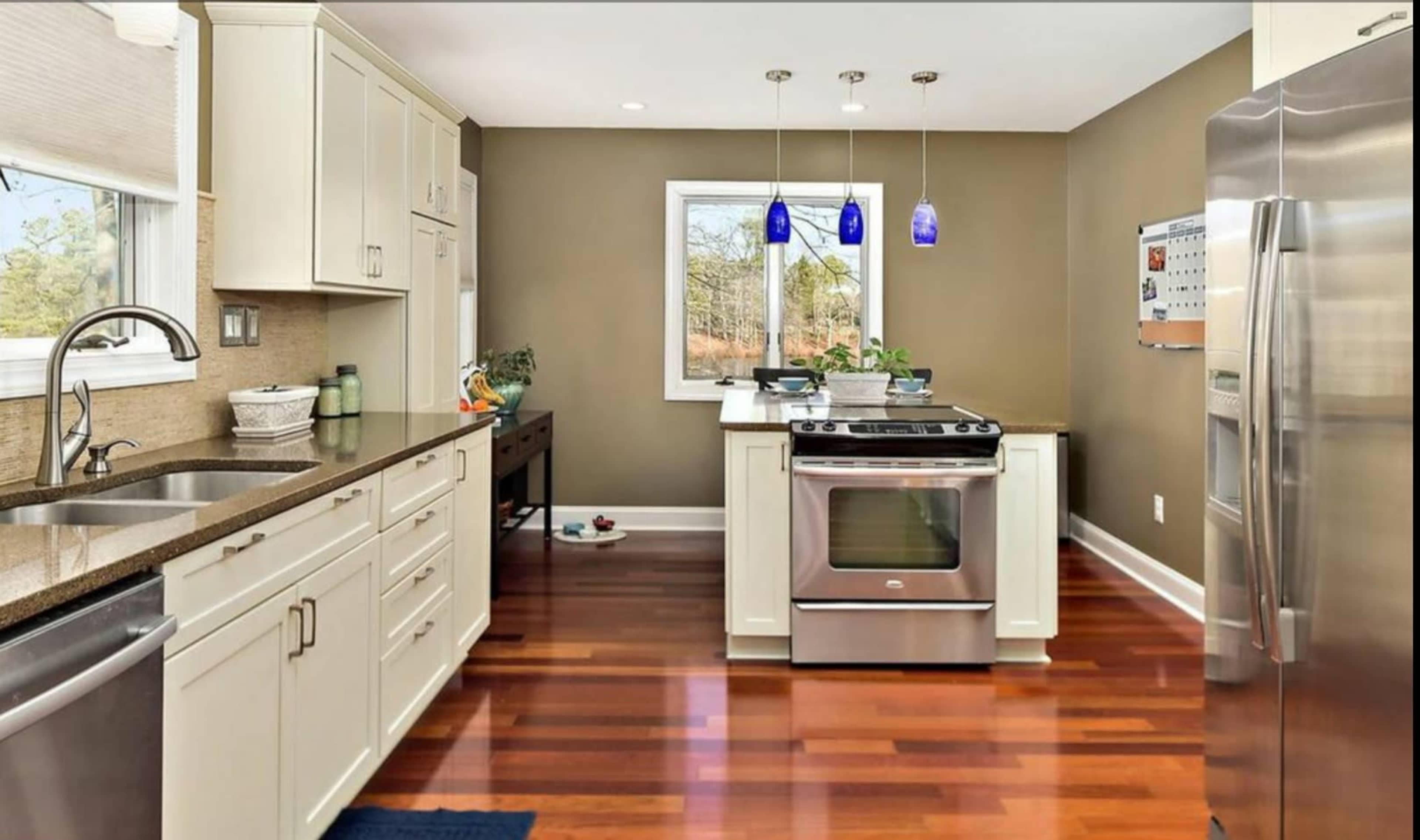 A modern kitchen with white cabinetry, stainless steel appliances, and dark wood flooring.