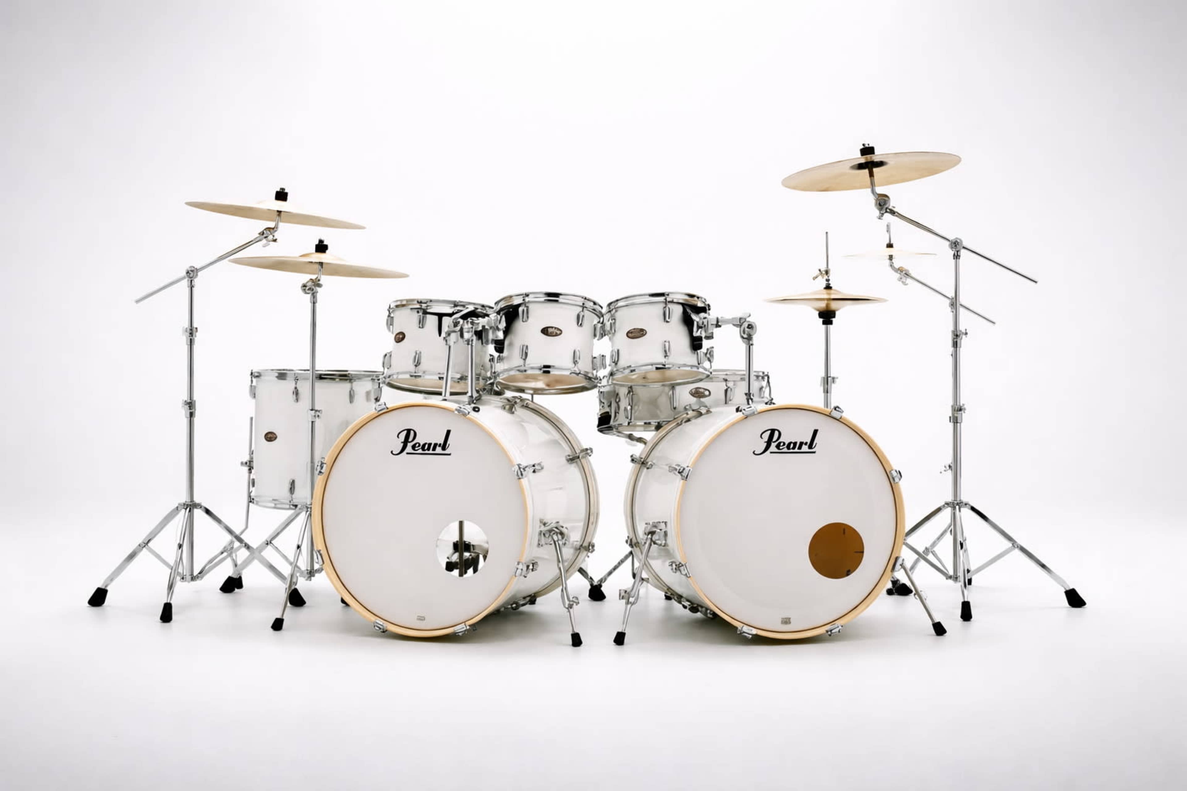 A white drum set with two bass drums, multiple toms, and two cymbals is positioned against a plain white backdrop.