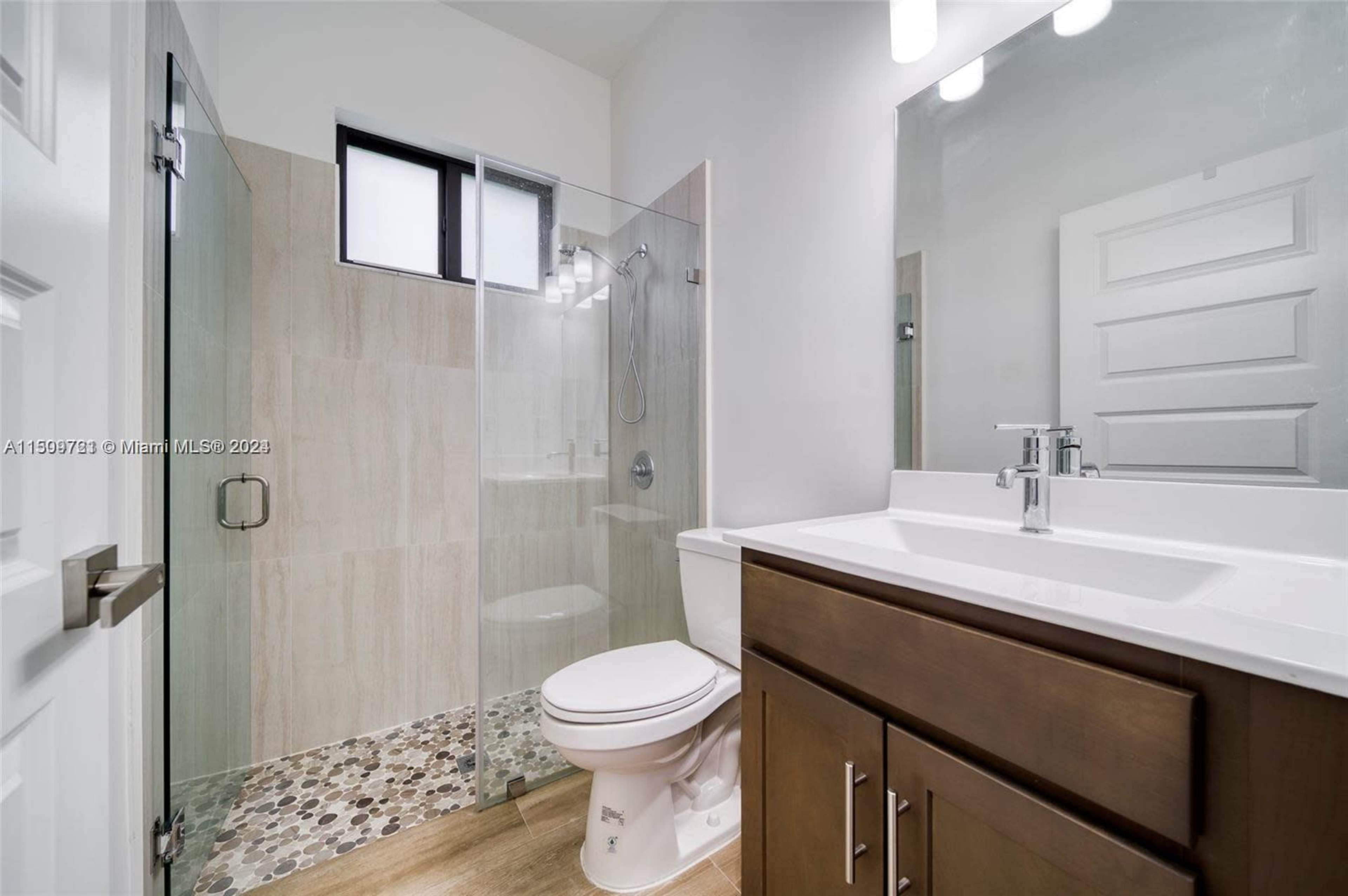 A modern bathroom featuring a glass shower enclosure, a white vanity with a sink, and a toilet.