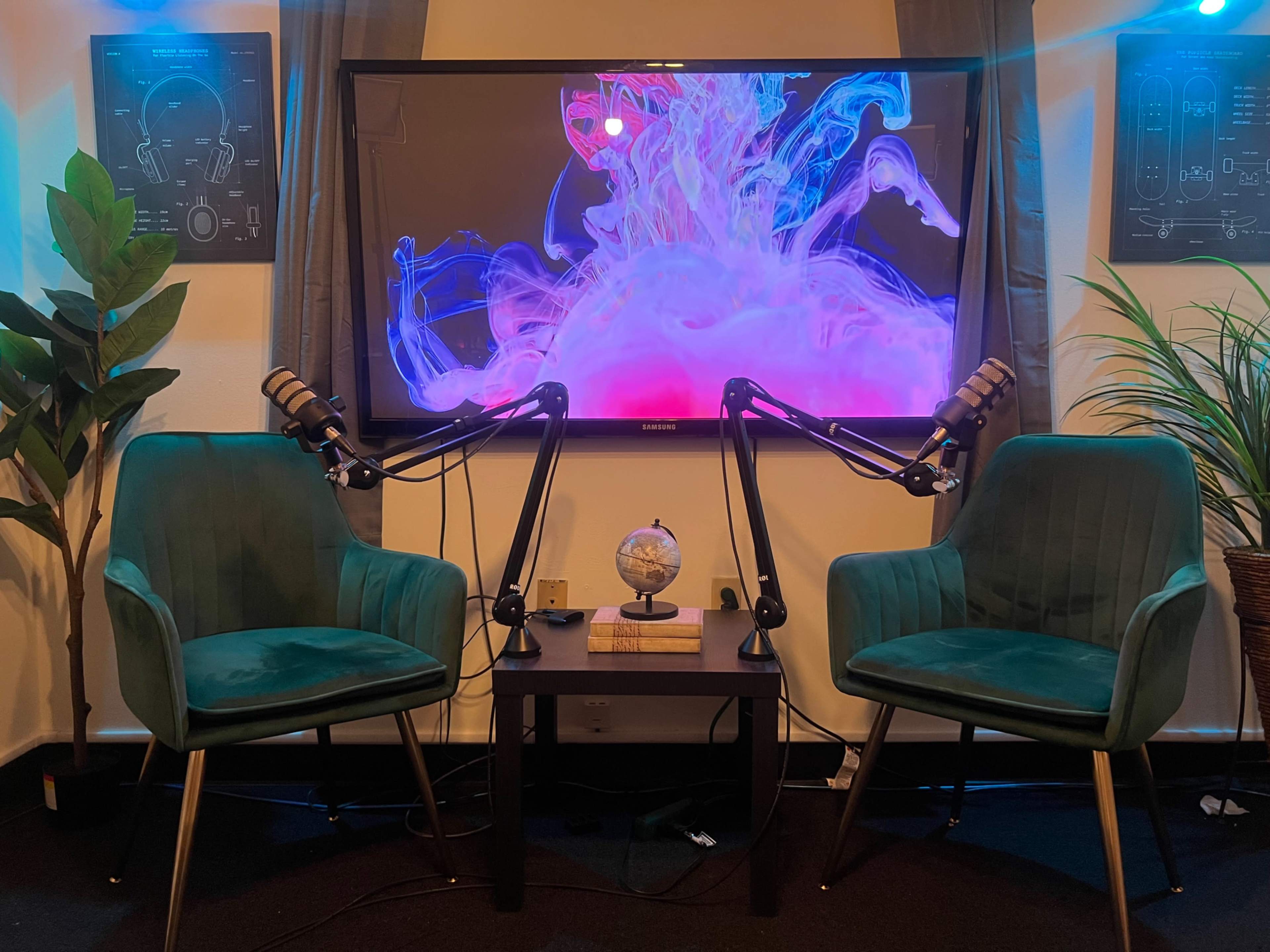A cozy studio setup features two green velvet chairs, a small globe on a table, and a large screen displaying colorful fluid graphics.