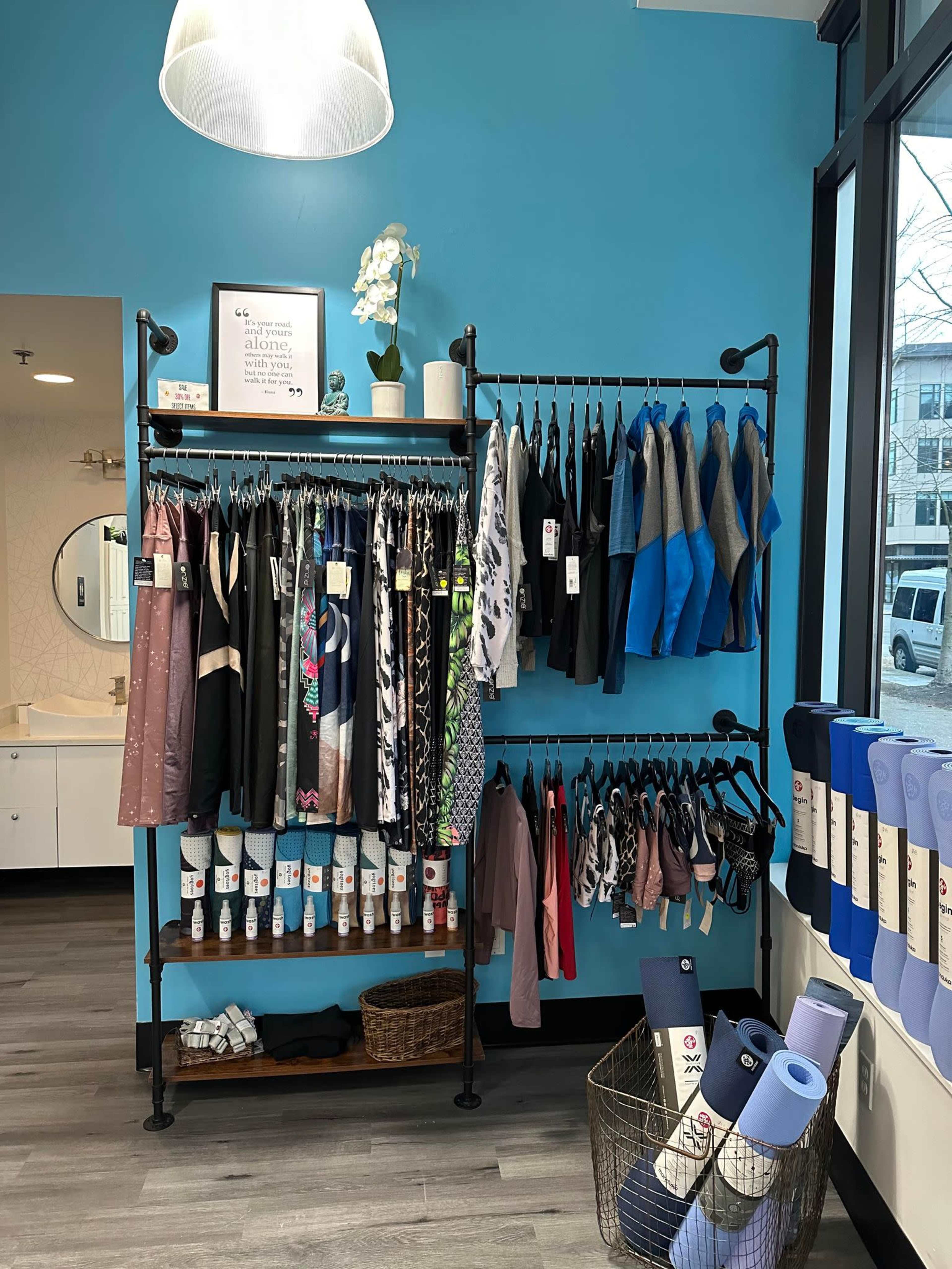 The image displays a clothing rack filled with various workout apparel and yoga mats arranged neatly against a blue wall in a store.