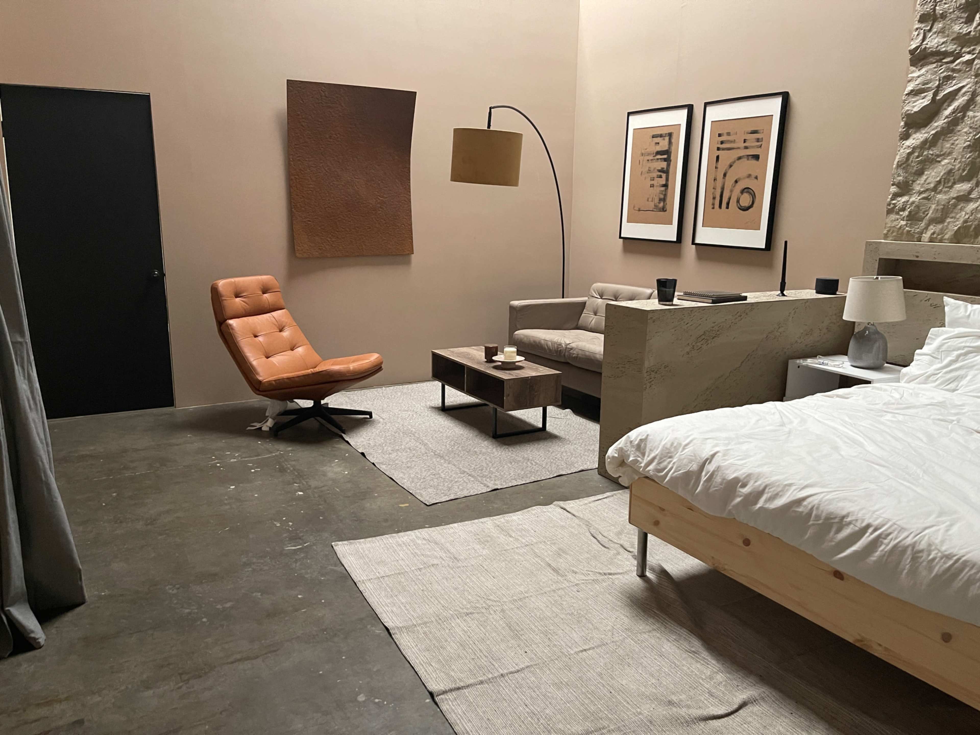 A modern bedroom with a bed, a brown armchair, a coffee table, and two framed artworks on the wall.