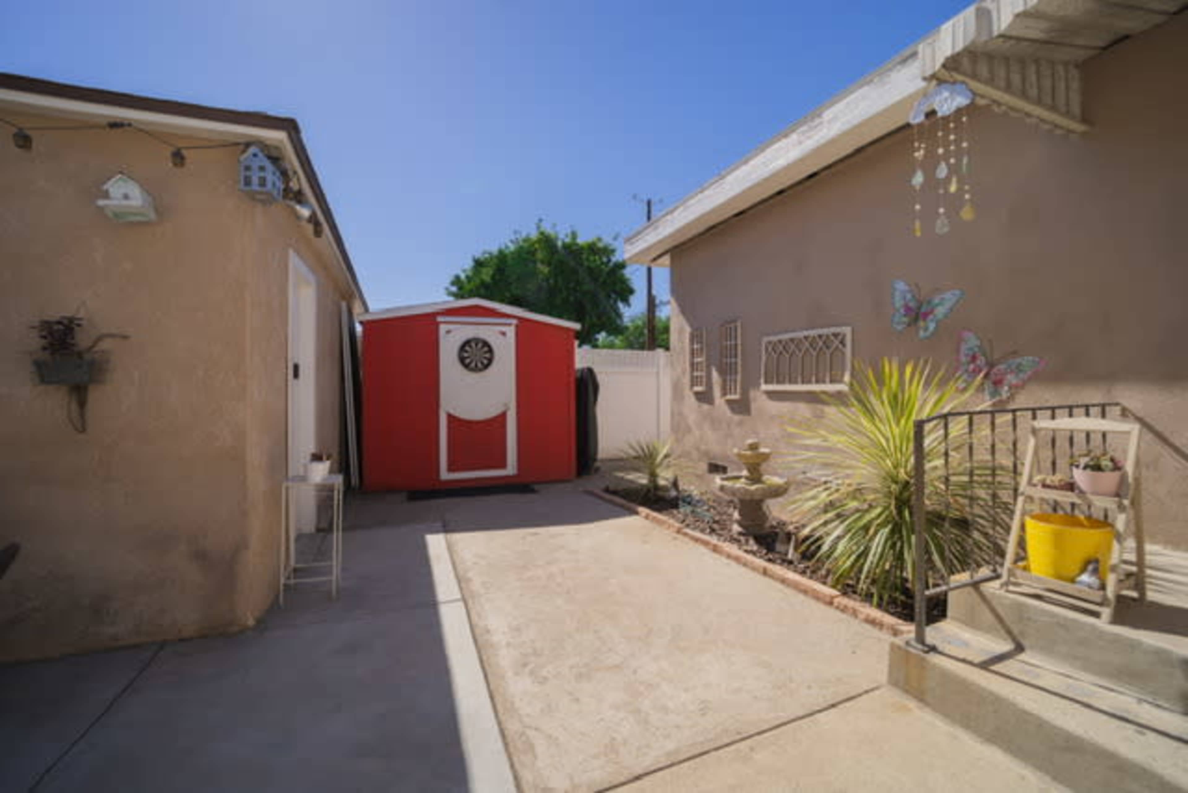 A small outdoor space with a red storage shed, a palm plant, and a staircase leading to a house with butterfly decorations on the wall.