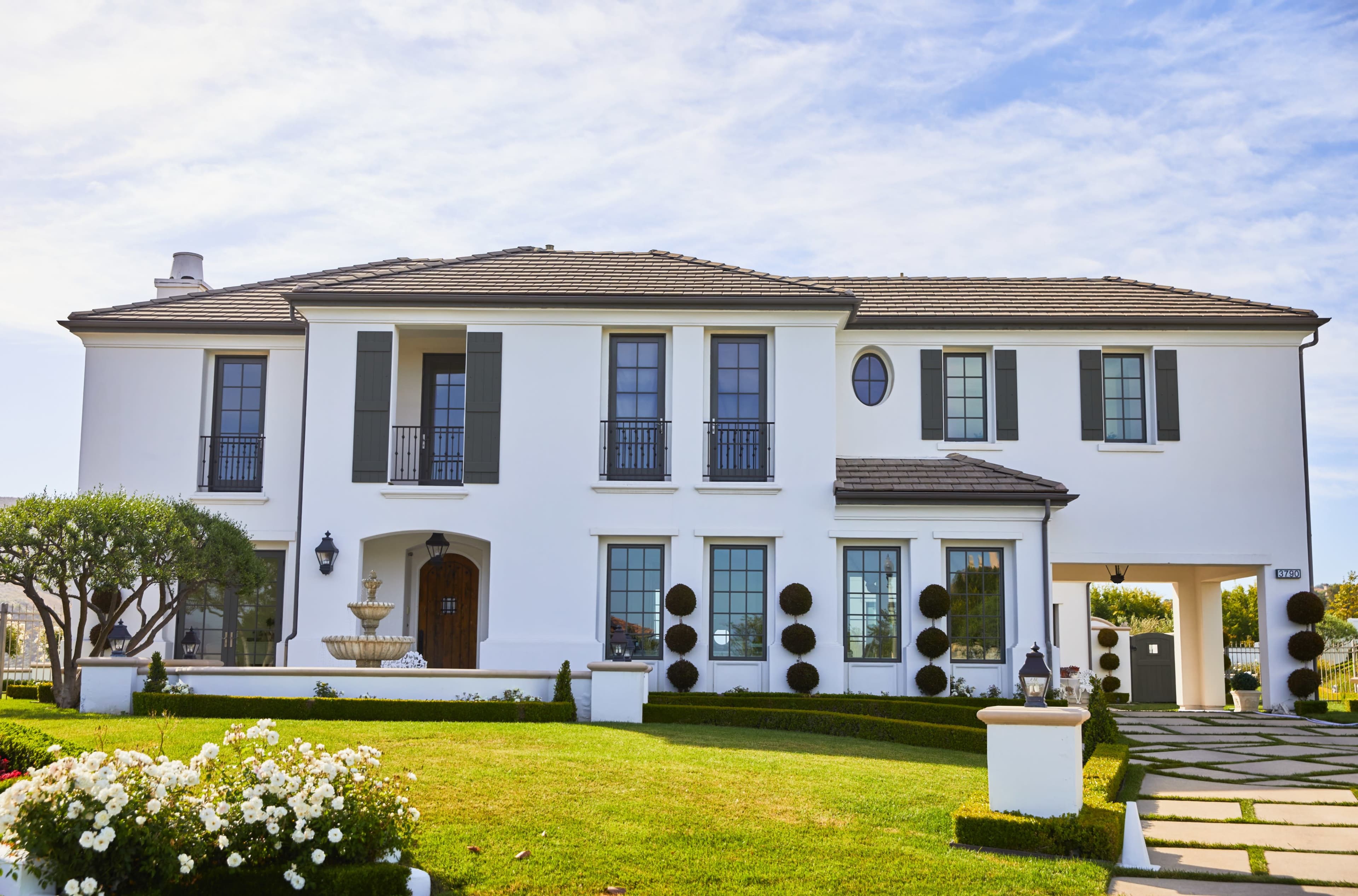 A two-story white house with a tiled roof, surrounded by neatly trimmed hedges and a well-maintained lawn.