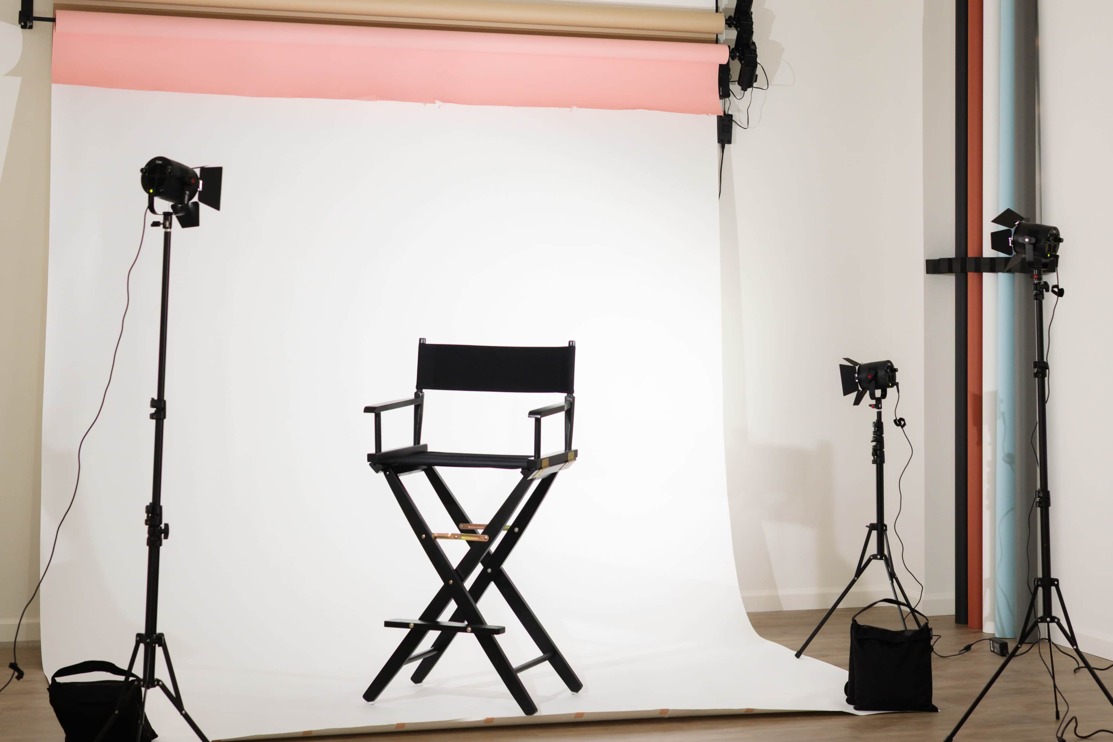 The image shows a director's chair positioned in front of a plain white backdrop, surrounded by studio lighting equipment.