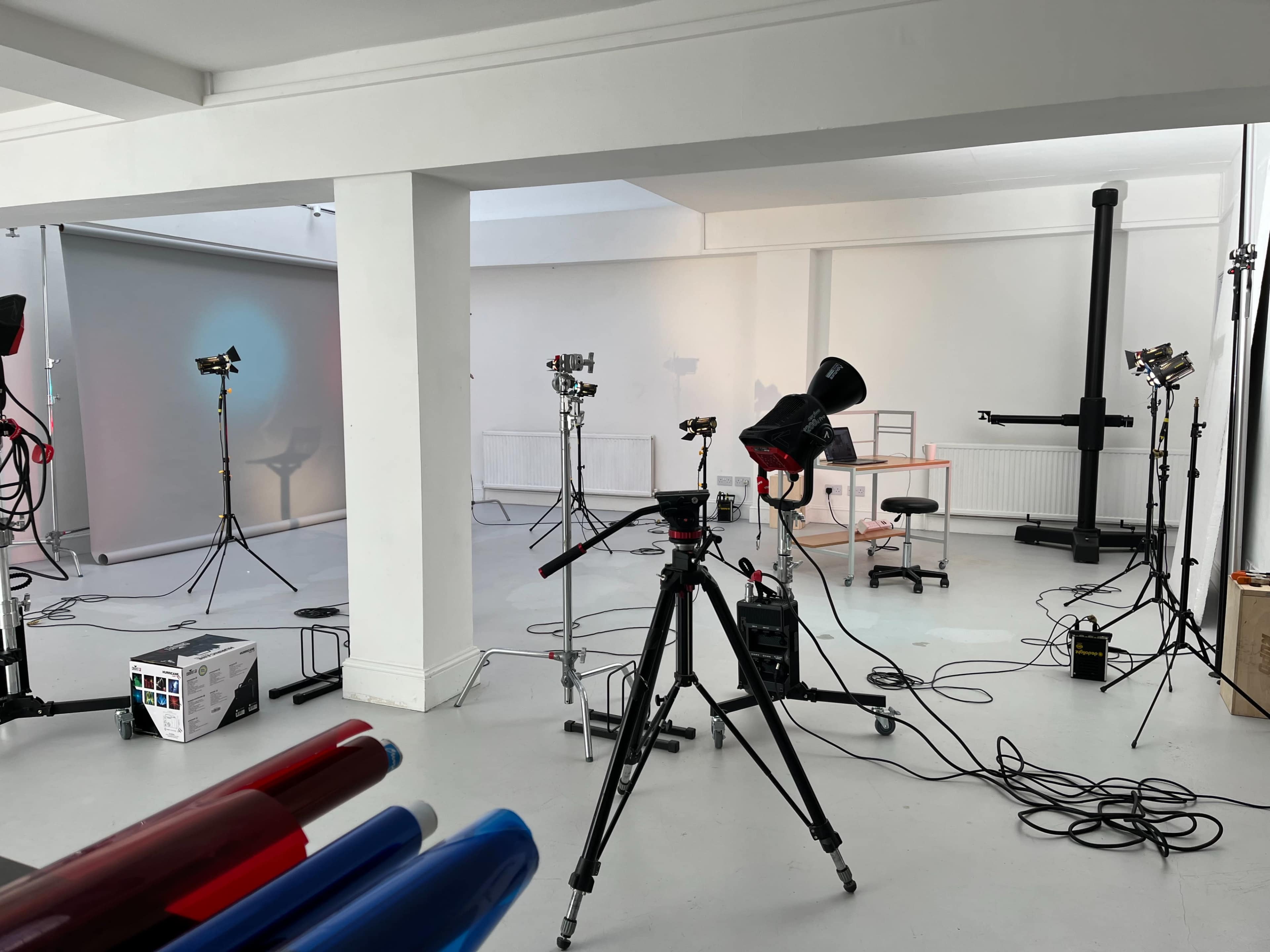 A photography studio is set up with tripods, lighting equipment, and a backdrop, surrounded by various tools and props.