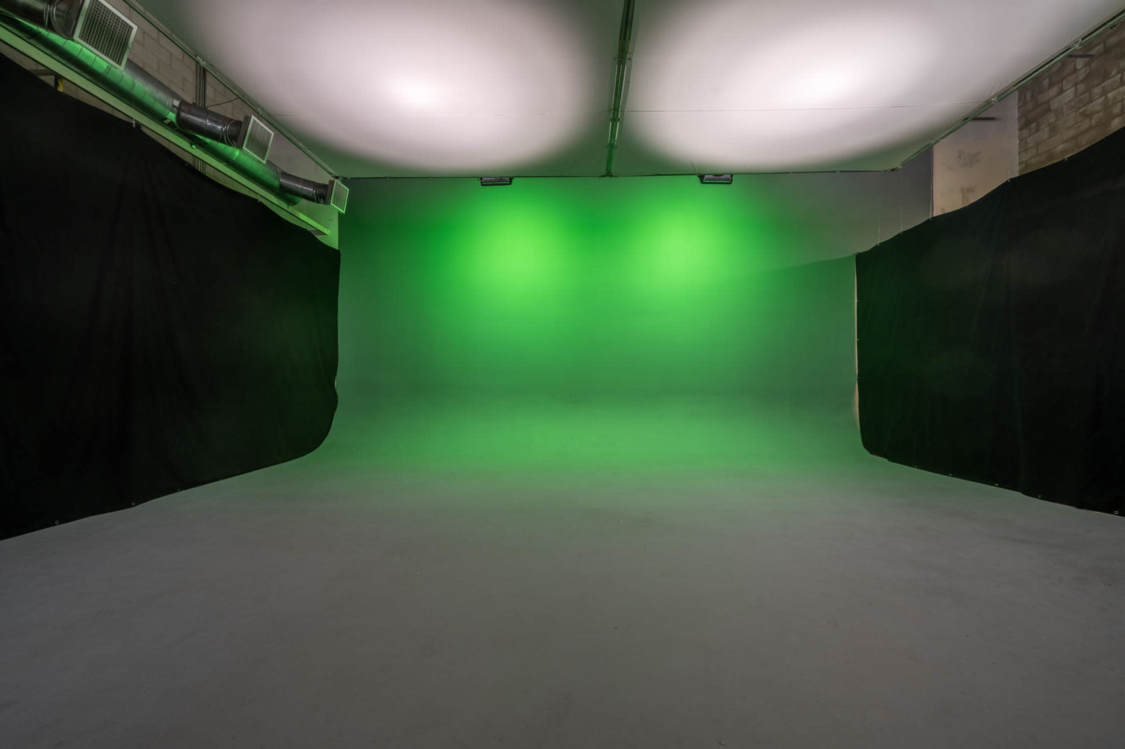 An empty studio space with a green backdrop and black drapes on either side.