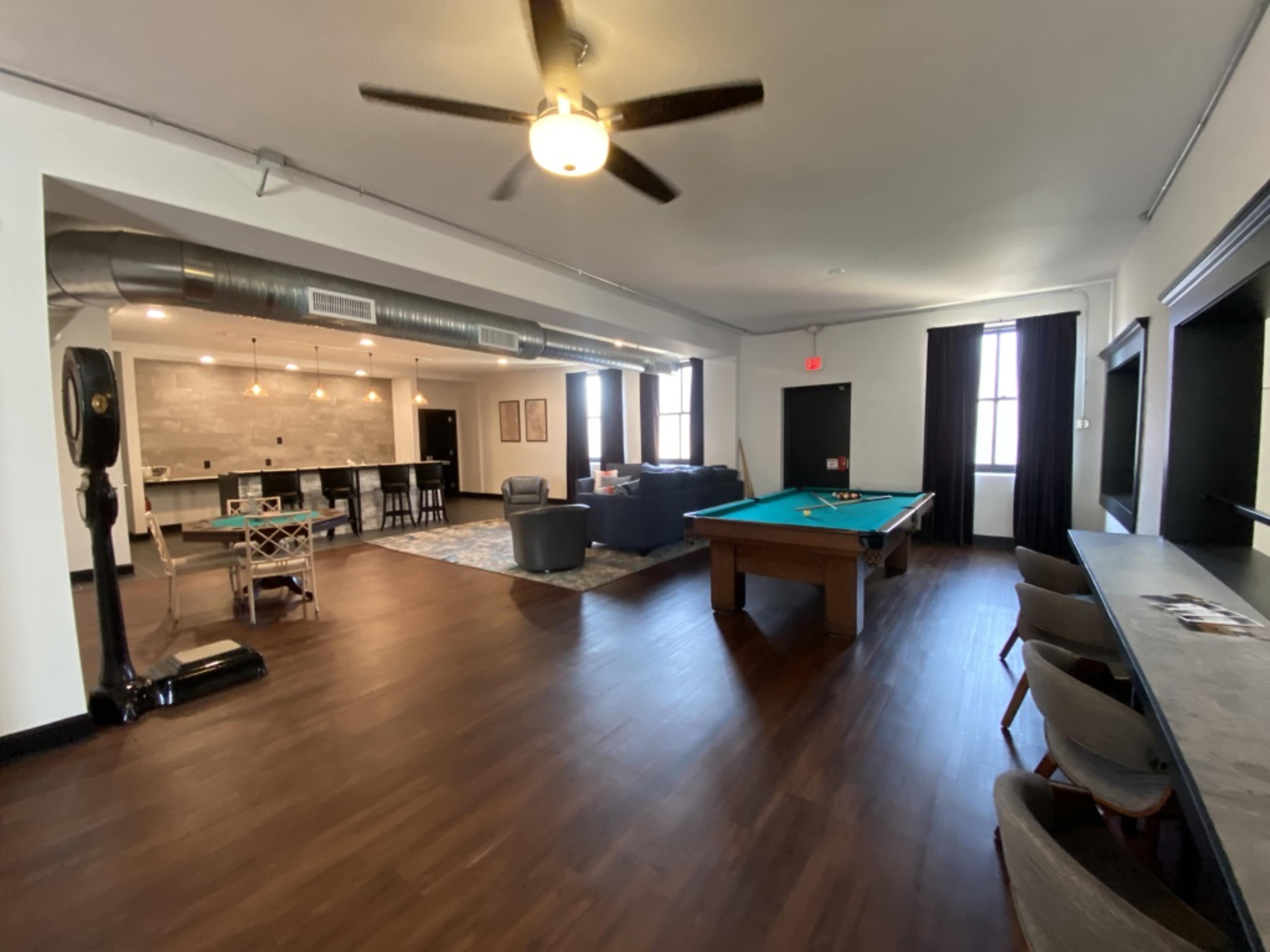 A spacious lounge area with a pool table, seating, and a kitchen space in the background.