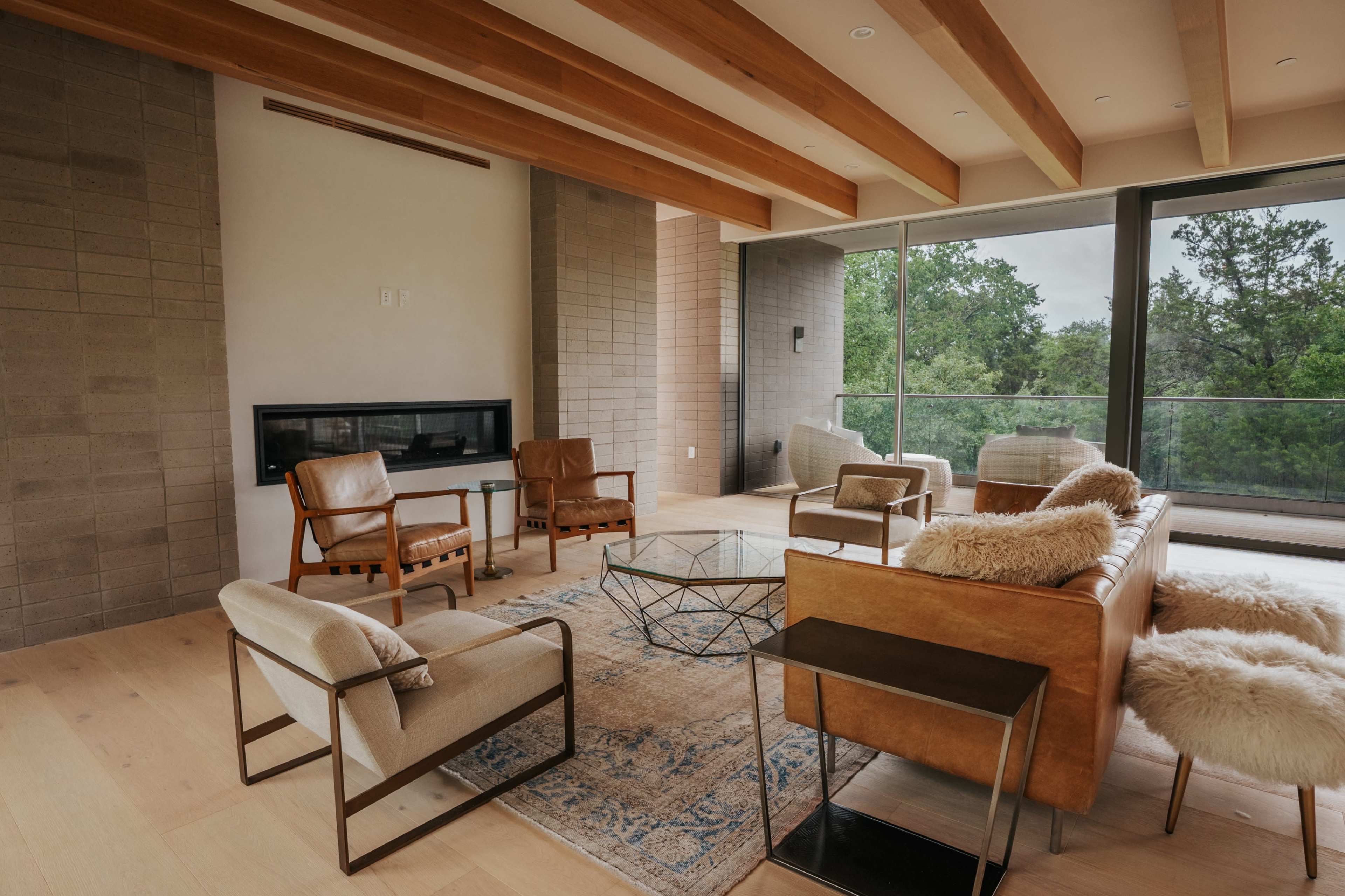 The image shows a modern living room with a large window, minimalist furniture, and wooden ceiling beams.