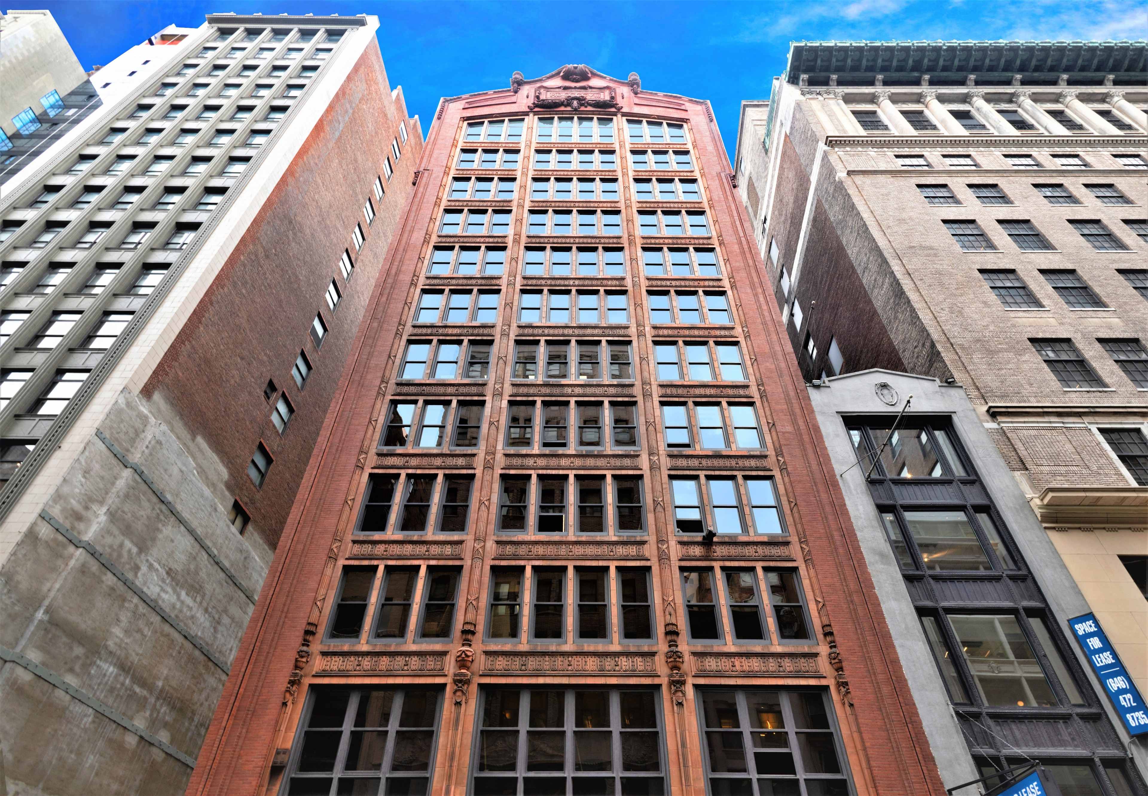 The image shows a row of tall buildings, prominently featuring a red brick structure with decorative elements and large windows.