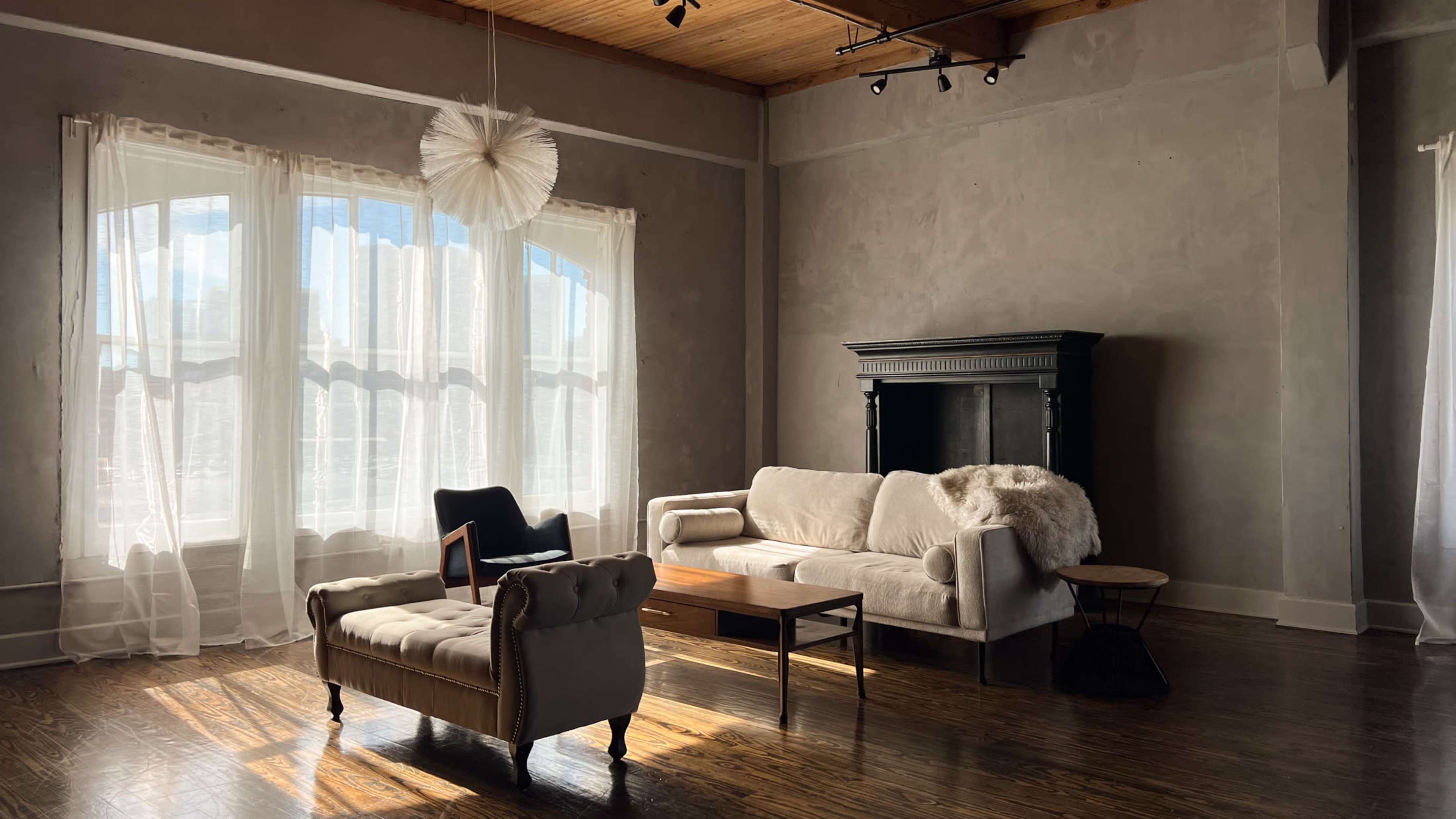 A modern living room features a light-colored sofa, a wooden coffee table, and a fireplace, with large windows allowing natural light to fill the space.