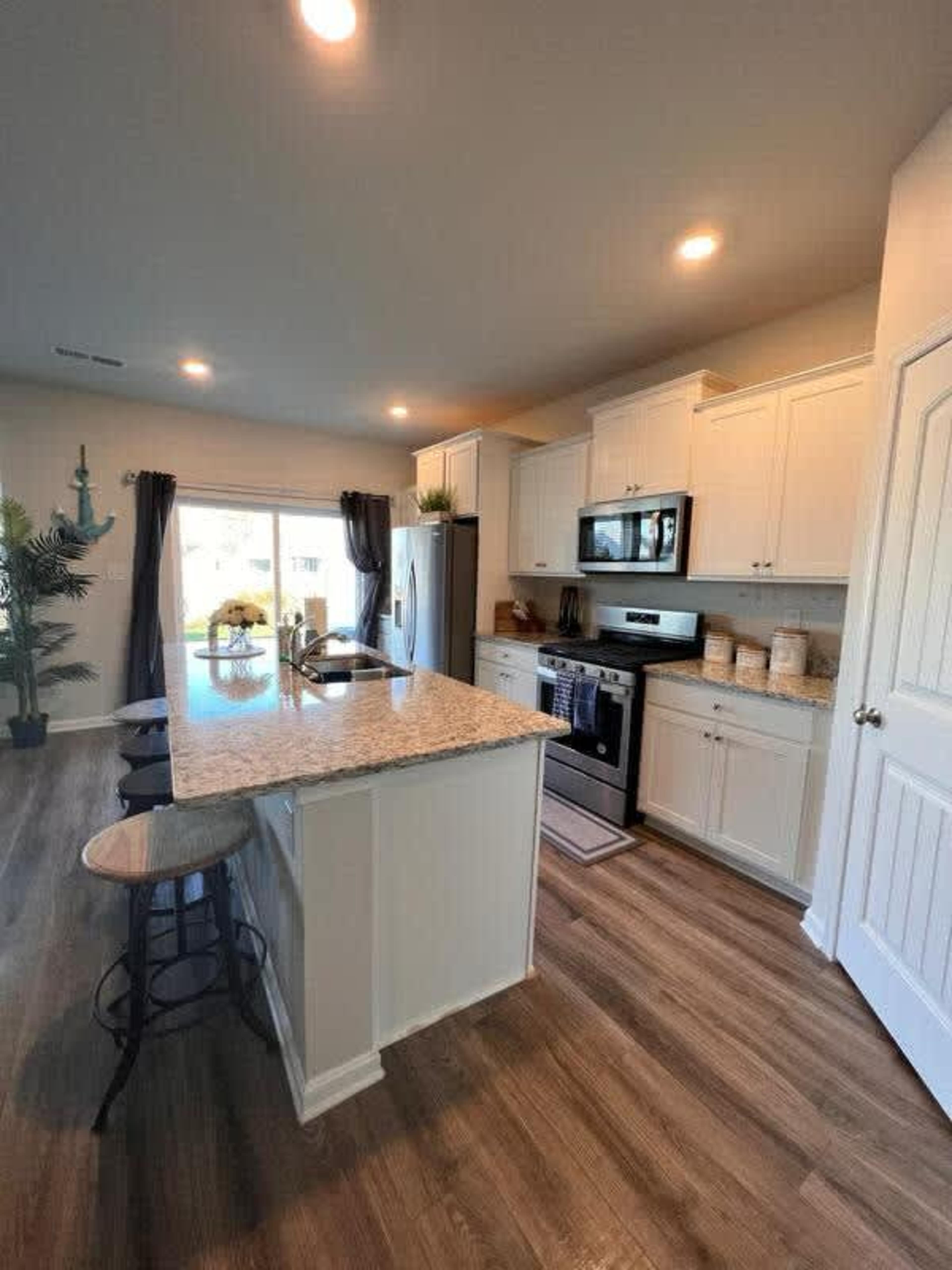 A modern kitchen with white cabinetry, stainless steel appliances, a granite countertop, and a spacious island with barstool seating.