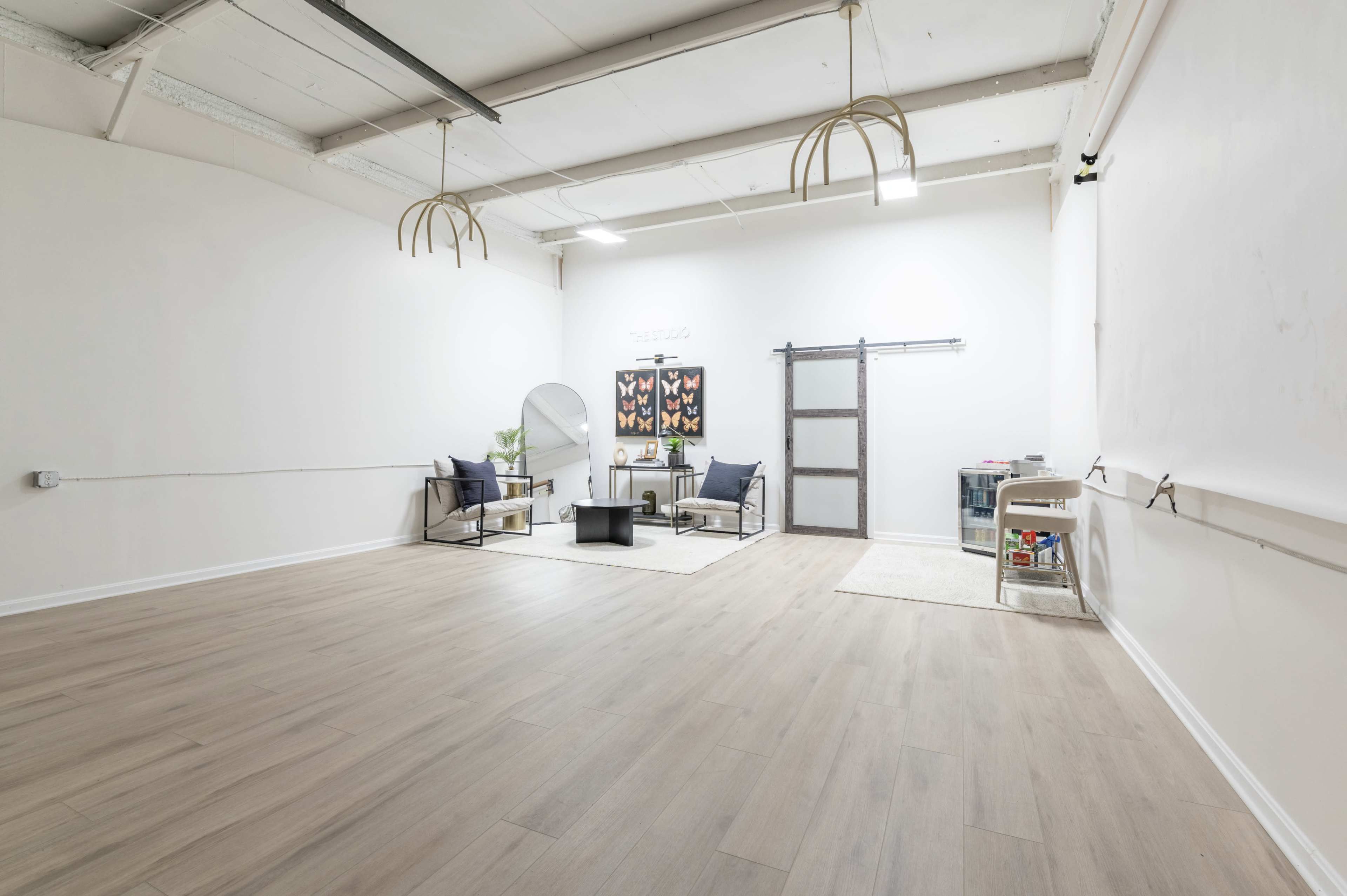 A spacious, empty room with wooden flooring, featuring minimal furniture, a large mirror, and a sliding door.