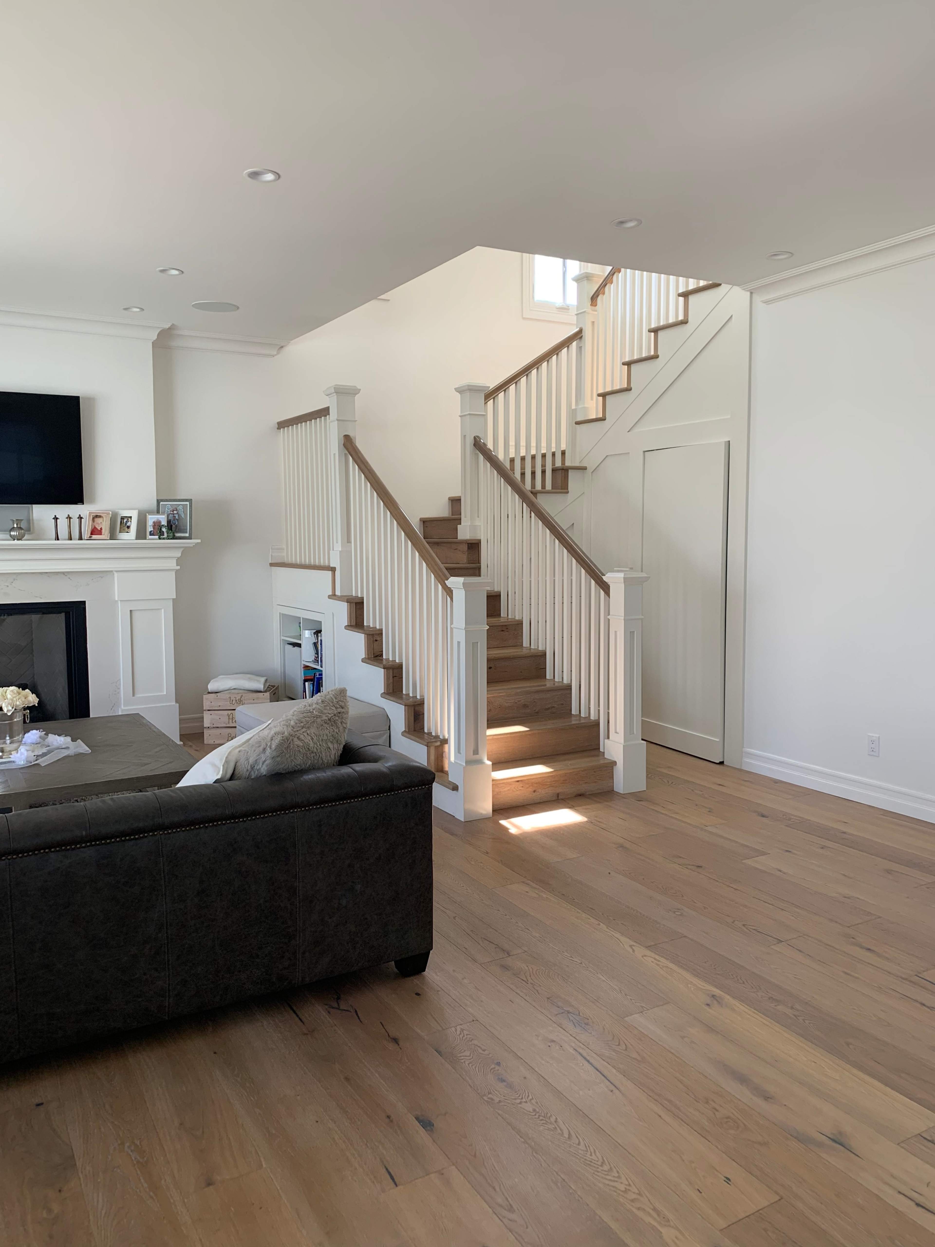 A modern living room with a staircase leading to an upper level, framed by white walls and wooden flooring.